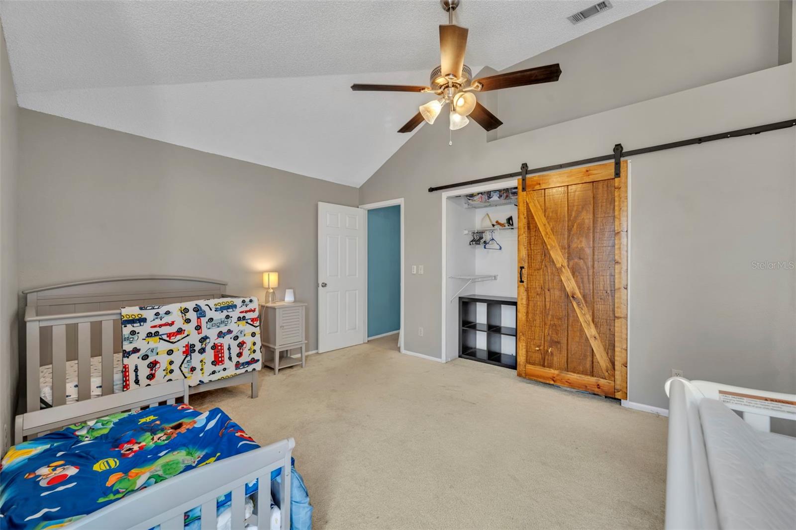 Spacious secondary bedroom with vaulted ceilings, neutral paint, and a stylish barn door accent leading to the closet. This bright and cheerful space offers room for multiple beds or a play area, making it perfect for a growing family, guest suite, or home office. Updated light fixture with ceiling fan adds both comfort and charm. Located just steps from the full bath and featuring ample natural light, this room is move-in ready and full of flexibility for any lifestyle - 2810 CORNERSTONE CT, APOPKA