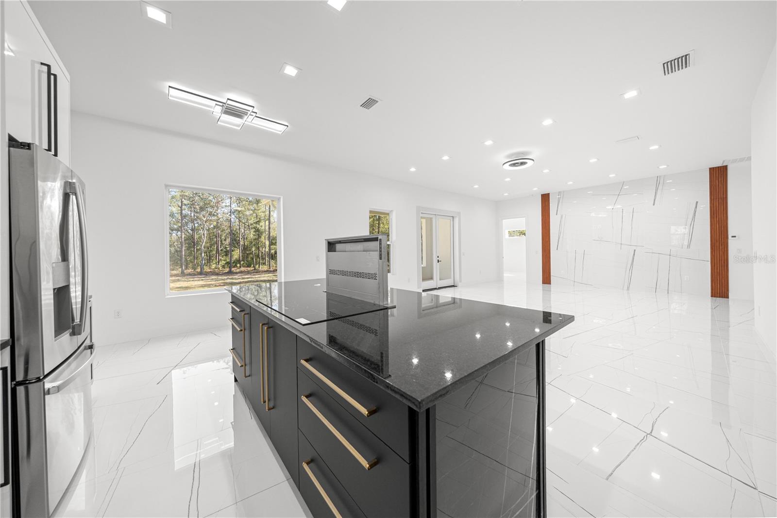 KITCHEN - GRANITE ISLAND - INDUCTION COOKTOP WITH DOWNDRAFT VENTILATION SYSTEM AND VIEW OF THE OPEN LIVING ROOM/DINING ROOM AREA - 6877 SW 131ST CIR, OCALA