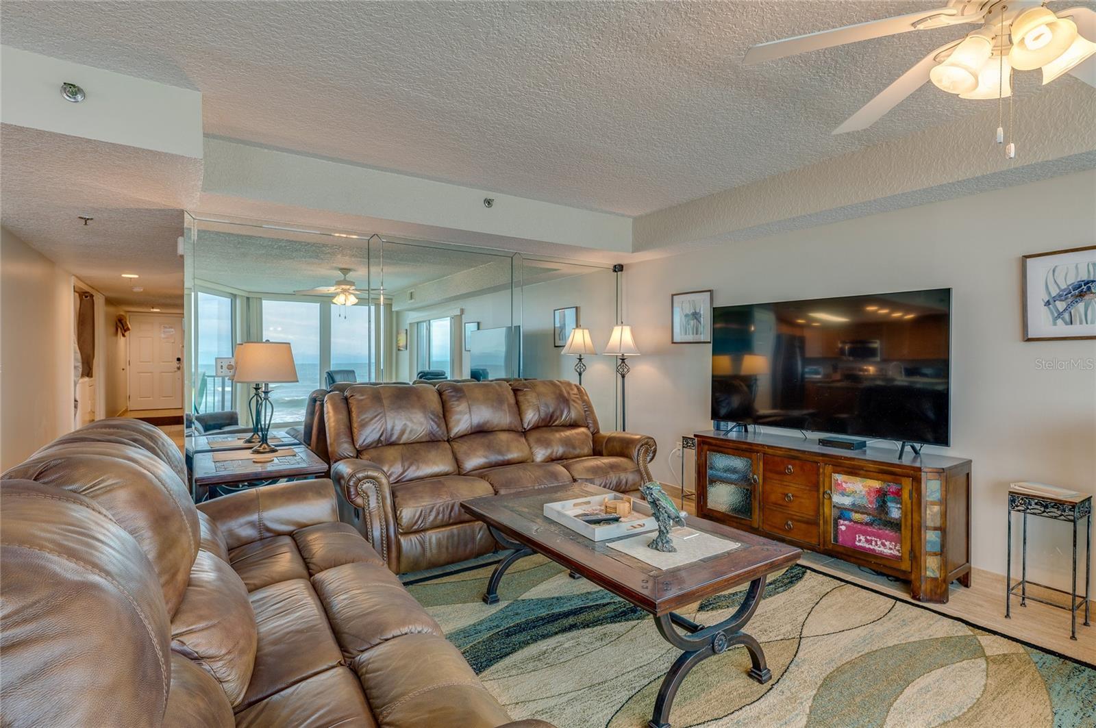 This angle captures the mirrored accent wall, recessed lighting, and an open-concept layout that seamlessly connects the living space with the kitchen and entryway. - 6727 TURTLEMOUND RD #315, NEW SMYRNA BEACH