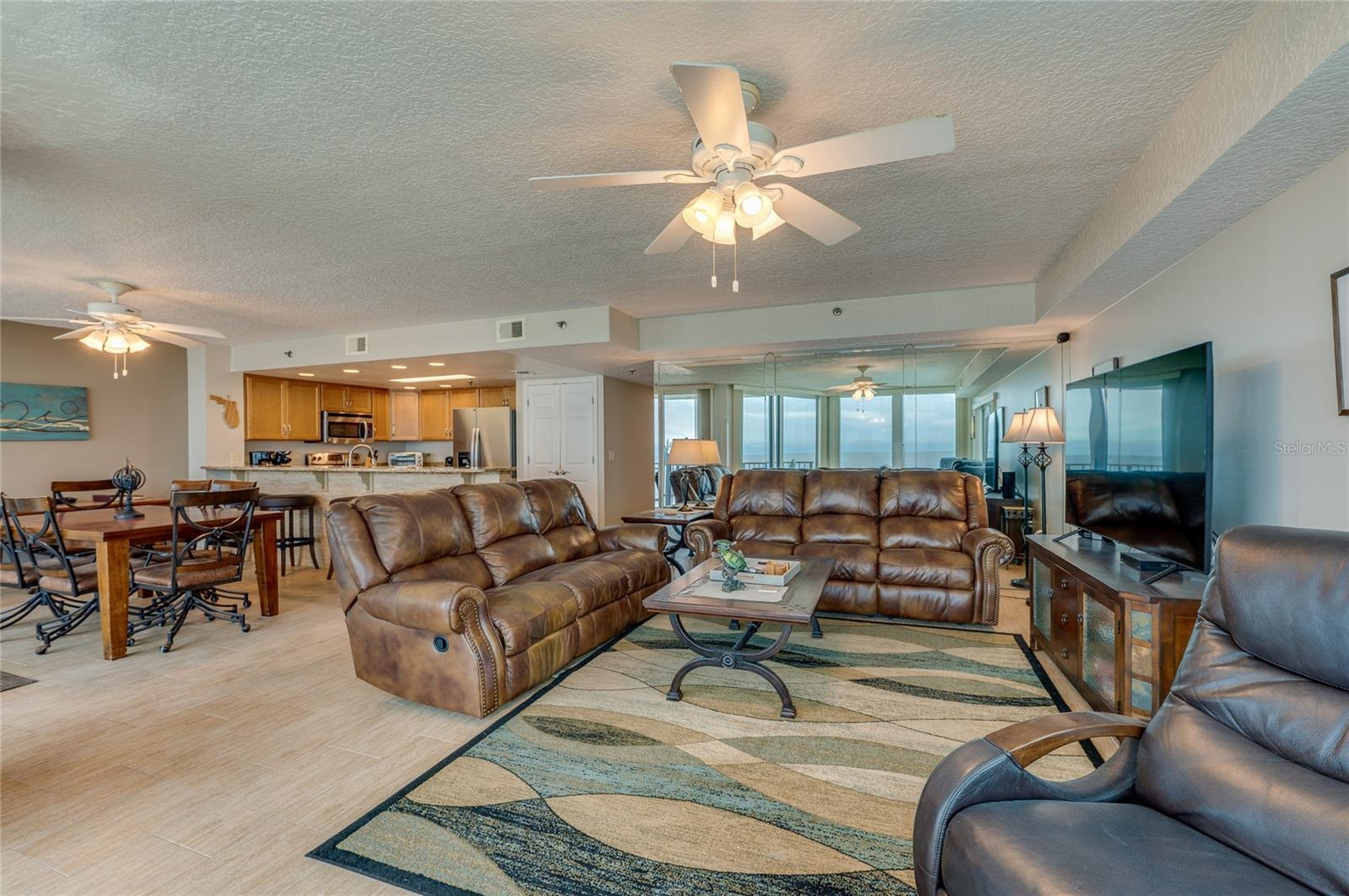 The spacious open-concept design combines living, dining, and kitchen areas, offering coastal views, recessed lighting, and a mirrored accent wall that enhances the natural light. - 6727 TURTLEMOUND RD #315, NEW SMYRNA BEACH