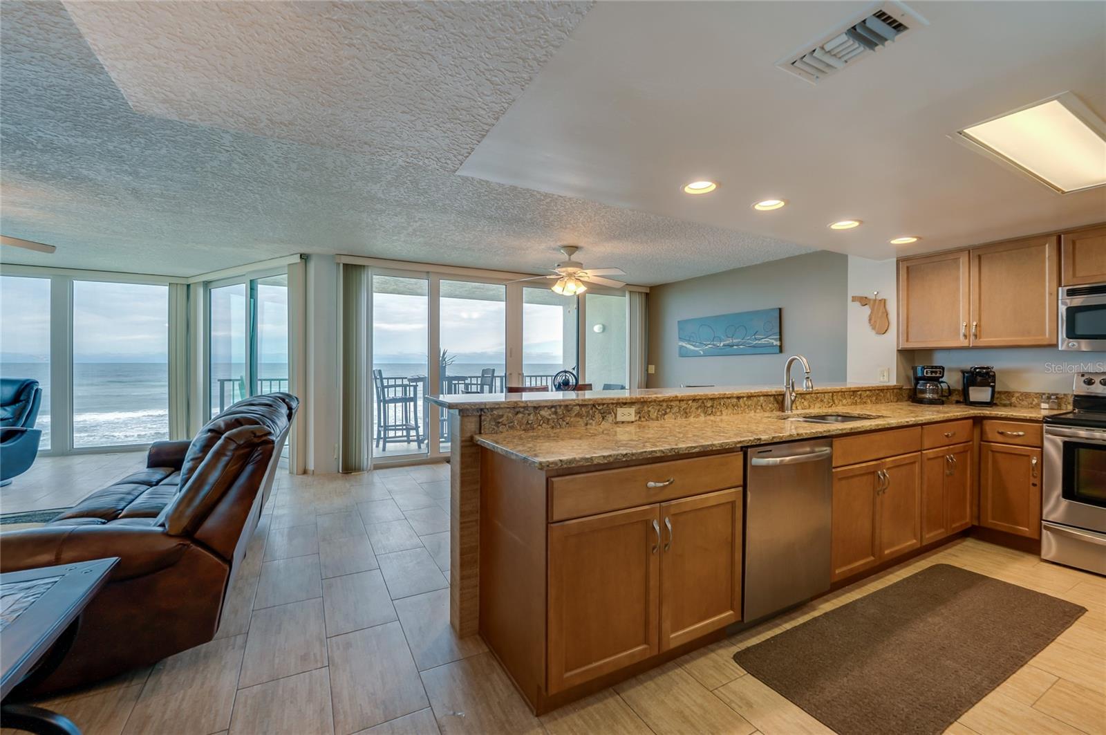 This open kitchen boasts granite countertops, stainless steel appliances, and a breakfast bar overlooking the ocean-facing dining space—perfect for entertaining or everyday living. - 6727 TURTLEMOUND RD #315, NEW SMYRNA BEACH