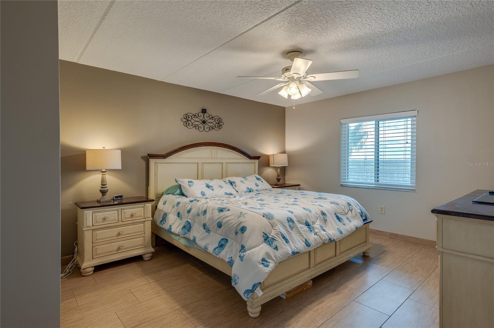 This spacious bedroom offers warm neutral tones, a ceiling fan for added comfort, and a large window that brings in natural light. The room’s layout allows for flexible furniture arrangements and a relaxed coastal ambiance. - 6727 TURTLEMOUND RD #315, NEW SMYRNA BEACH