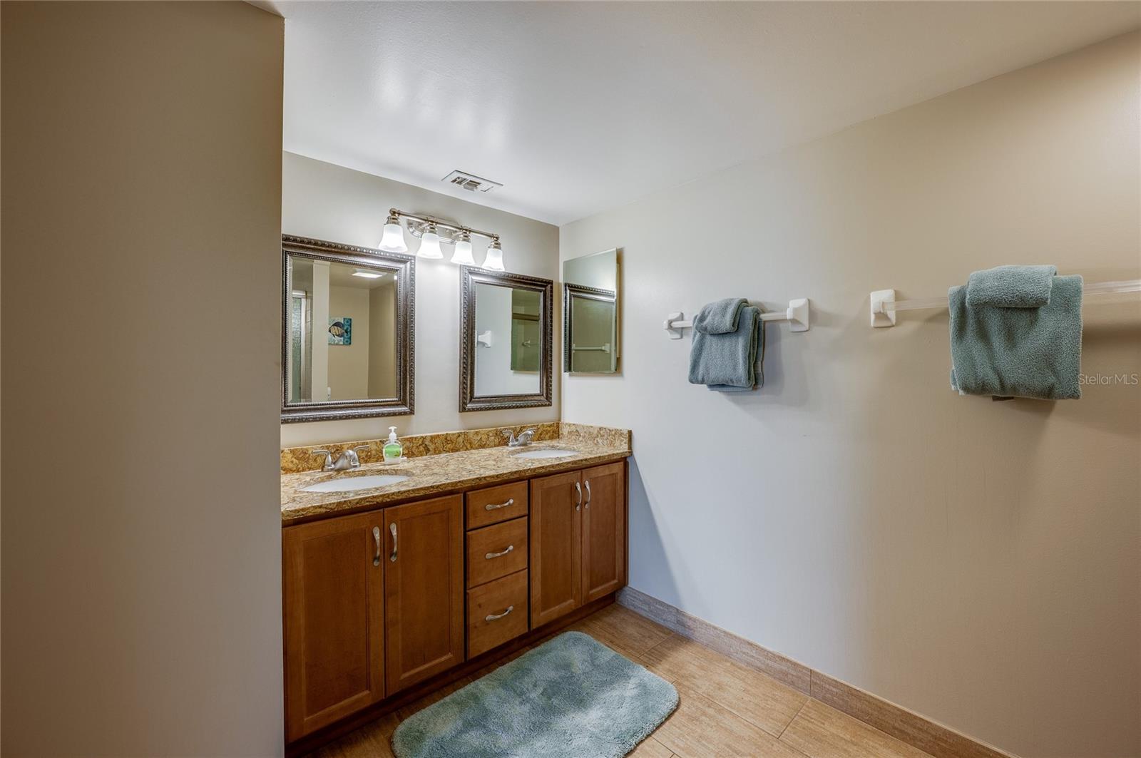 Dual mirrors with elegant framing and granite countertops top the double vanity, offering plenty of storage in warm wood cabinetry. - 6727 TURTLEMOUND RD #315, NEW SMYRNA BEACH