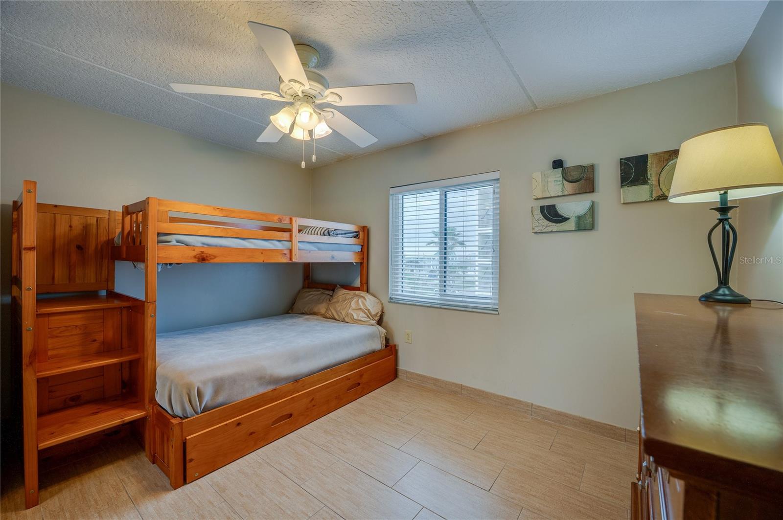 A bright and versatile second bedroom featuring tile flooring, a ceiling fan, and a large window for natural light—perfect for guests, a home office, or flexible living needs. - 6727 TURTLEMOUND RD #315, NEW SMYRNA BEACH