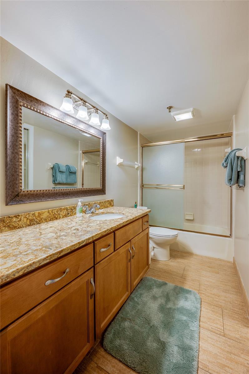 This full bath features a combination tub/shower with sliding doors, granite-look vanity, and framed mirror great for guests or shared use. - 6727 TURTLEMOUND RD #315, NEW SMYRNA BEACH