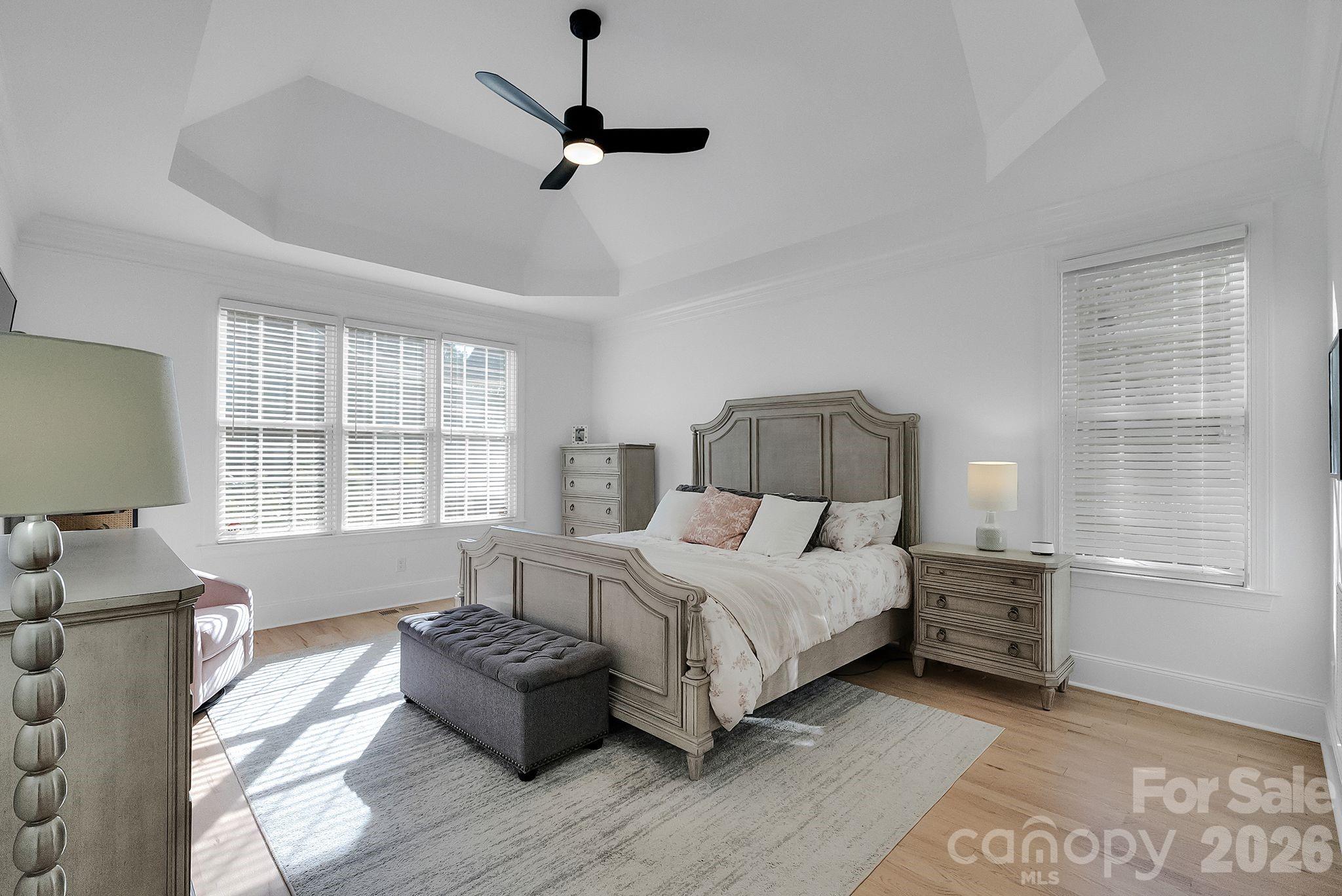 Spacious primary bedroom featuring a tray ceiling, ceiling fan, and abundant natural light. Soft finishes and generous layout create a comfortable retreat. - 7778 Burning Ridge Drive, Stanley