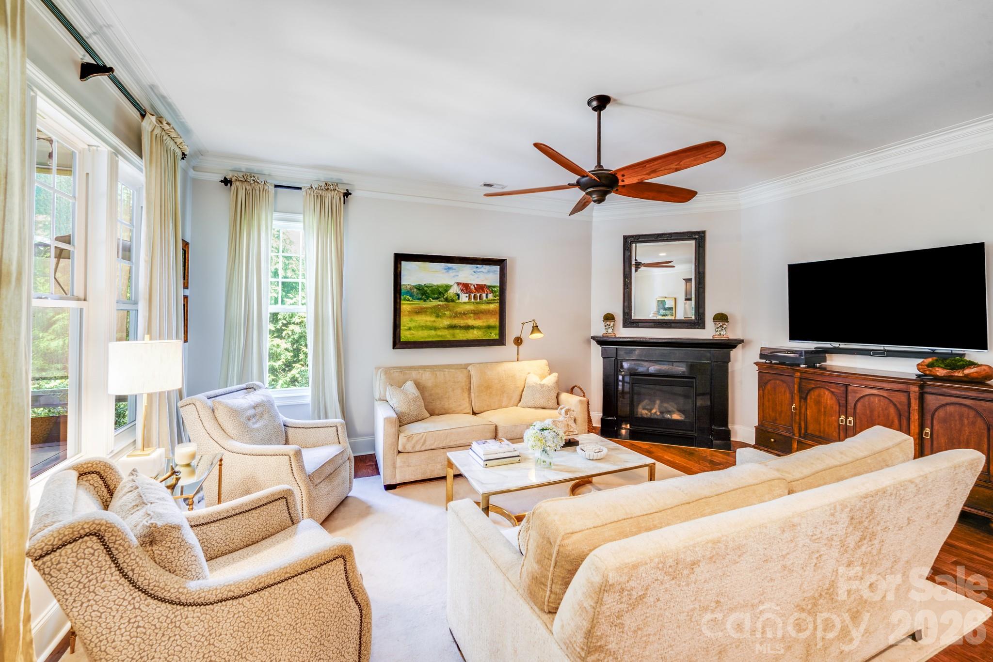 Gas fireplace with a black surround & mantel, crisp white crown molding and elegant ceiling fan with wood blades - 2702 Arsdale Road, Waxhaw