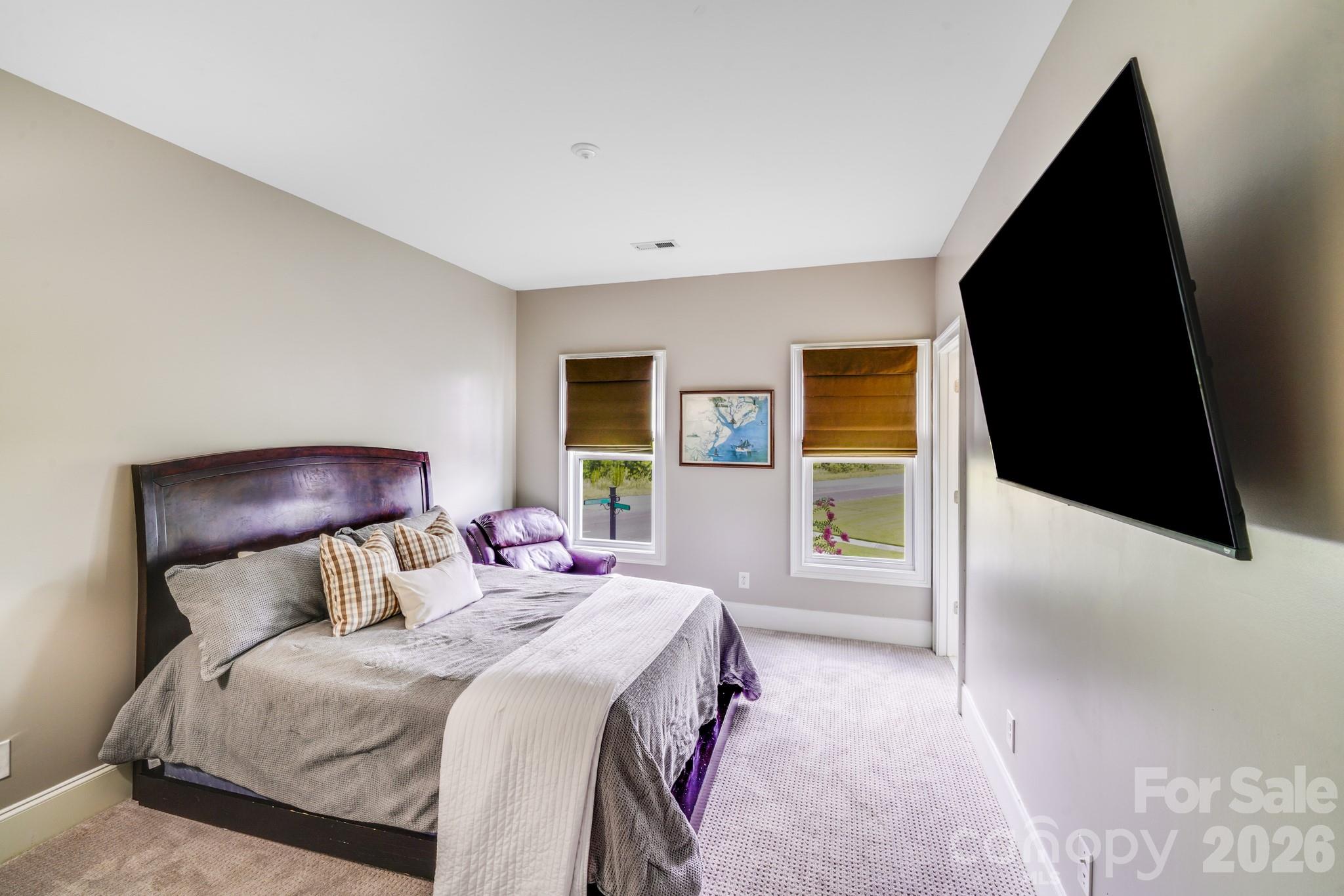 This inviting secondary bedroom features plush carpeting, blackout shades, a wall-mounted TV, and an ensuite bath - 2702 Arsdale Road, Waxhaw