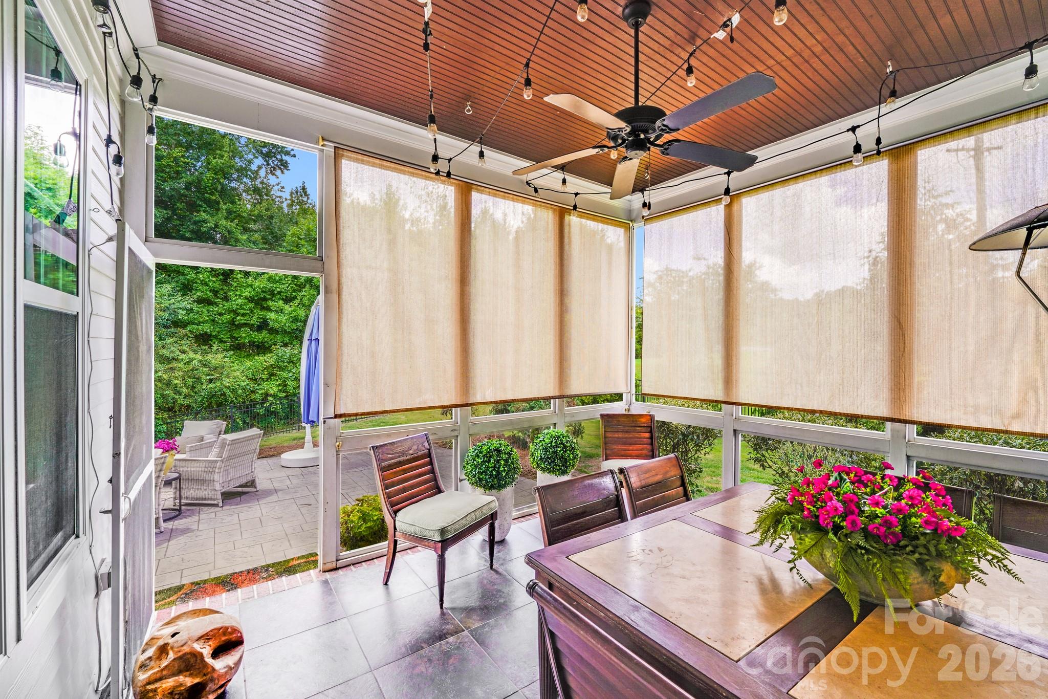 Inviting screened porch features slate tile flooring, stained wood ceiling with fan, café lights, & roll-down shades, offering a charming, private retreat that flows seamlessly onto the adjacent patio - 2702 Arsdale Road, Waxhaw