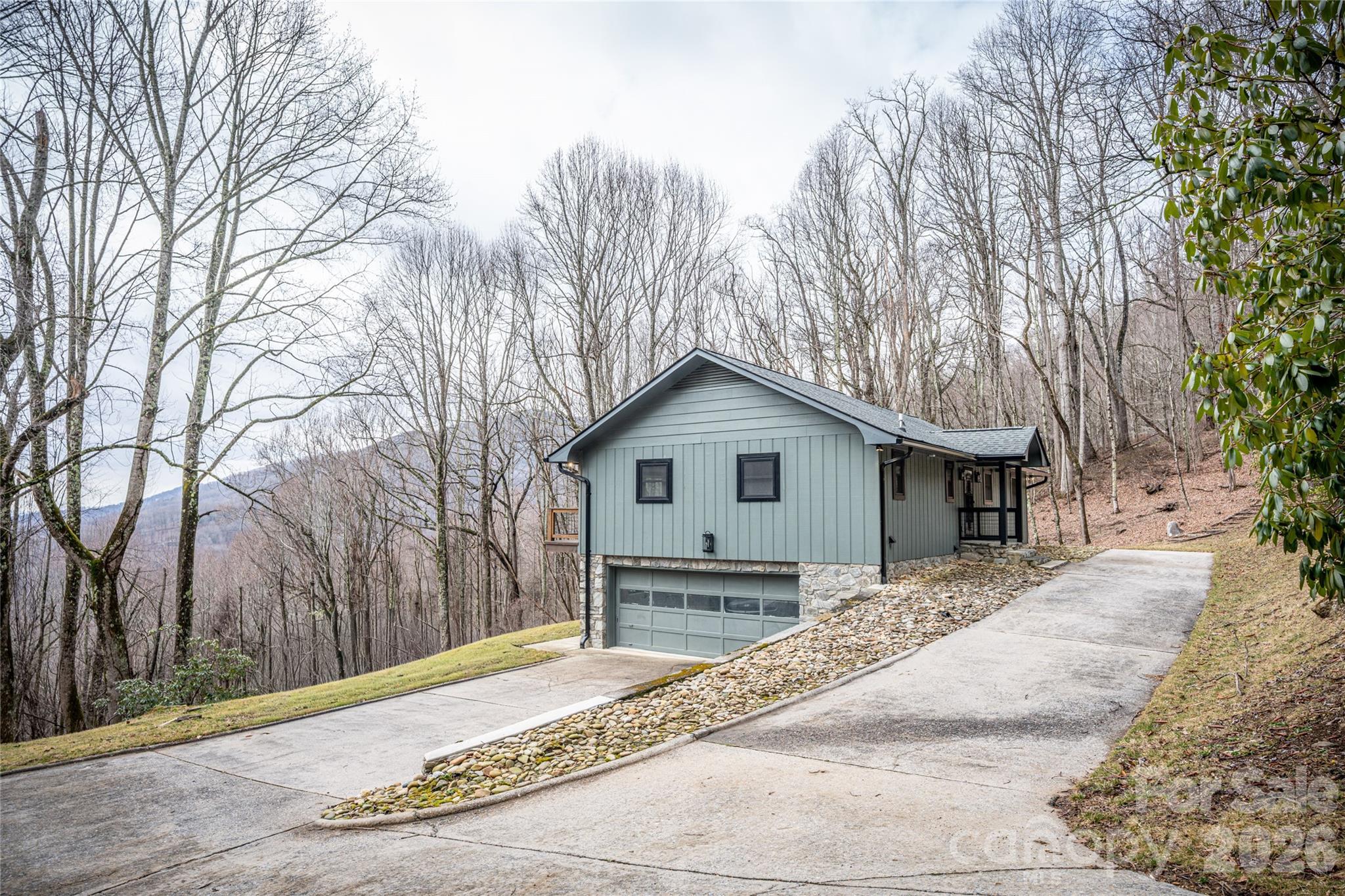 Long concrete driveway provides ample parking and easy access to the two-car garage. Stone foundation details and updated exterior finishes highlight the home’s complete renovation. - 453 Friendly Acres Drive, Waynesville