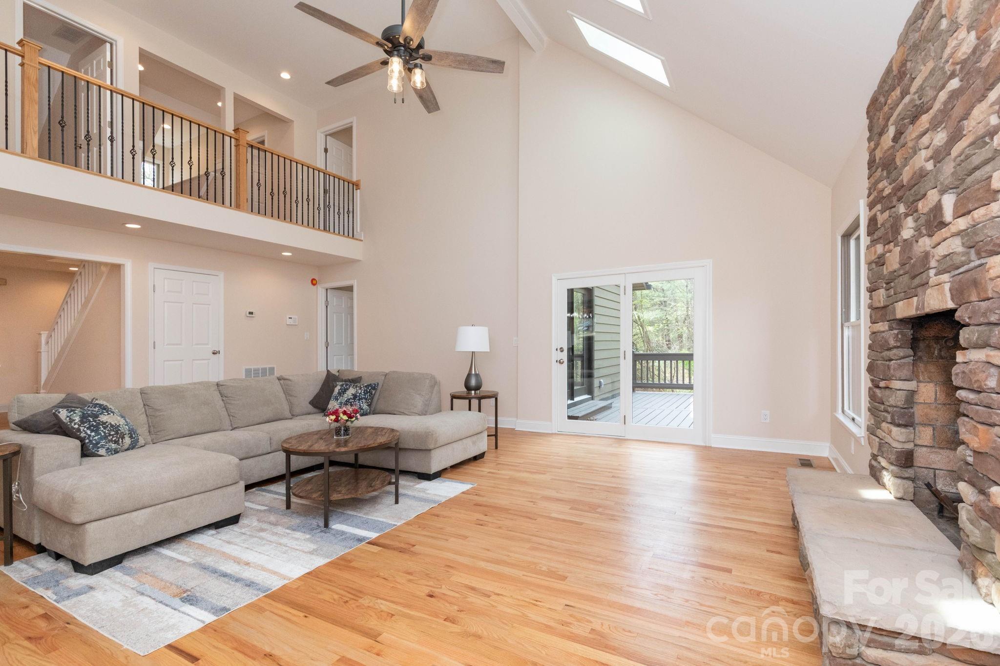 Spacious living room with soaring vaulted ceilings, skylights, and a stunning floor-to-ceiling stone fireplace. - 68 Sigmon Road, Fletcher