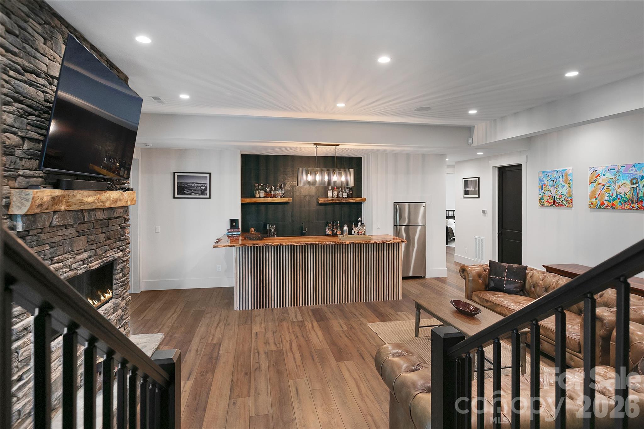 Designed for entertaining, the lower level family room offers the perfect gathering space with a striking stone fireplace and a handcrafted wood bar topped with a live edge countertop. - 726 Ugugu Drive, Brevard