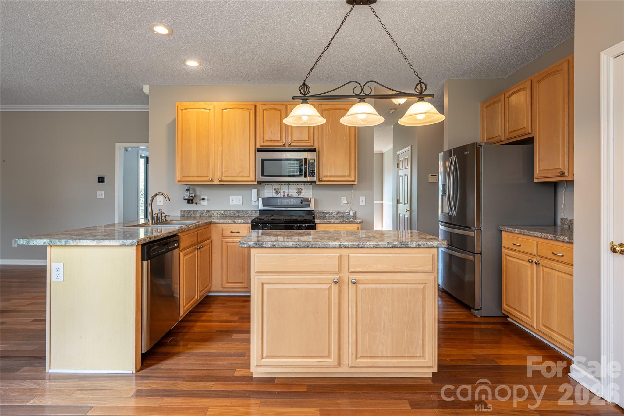 Kitchen with center island, breakfast bar, gas range, stainless appliances, pantry and pendant lighting; opens to family room and breakfast area. Natural gas, city water and sewer. - 48 Brownstone Court, Fletcher