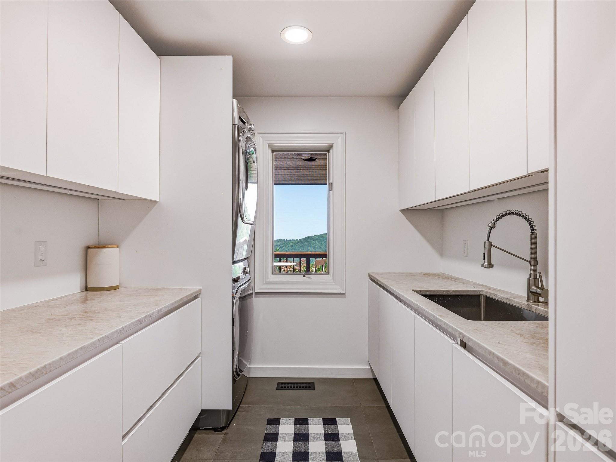 Laundry room with pocket door entry, recessed lighting, custom cabinetry & under cabinet lighting, Taj Mahal quartzite countertops, tile flooring and LG stacked washer and dryer. - 100 Big Spring Drive, Asheville