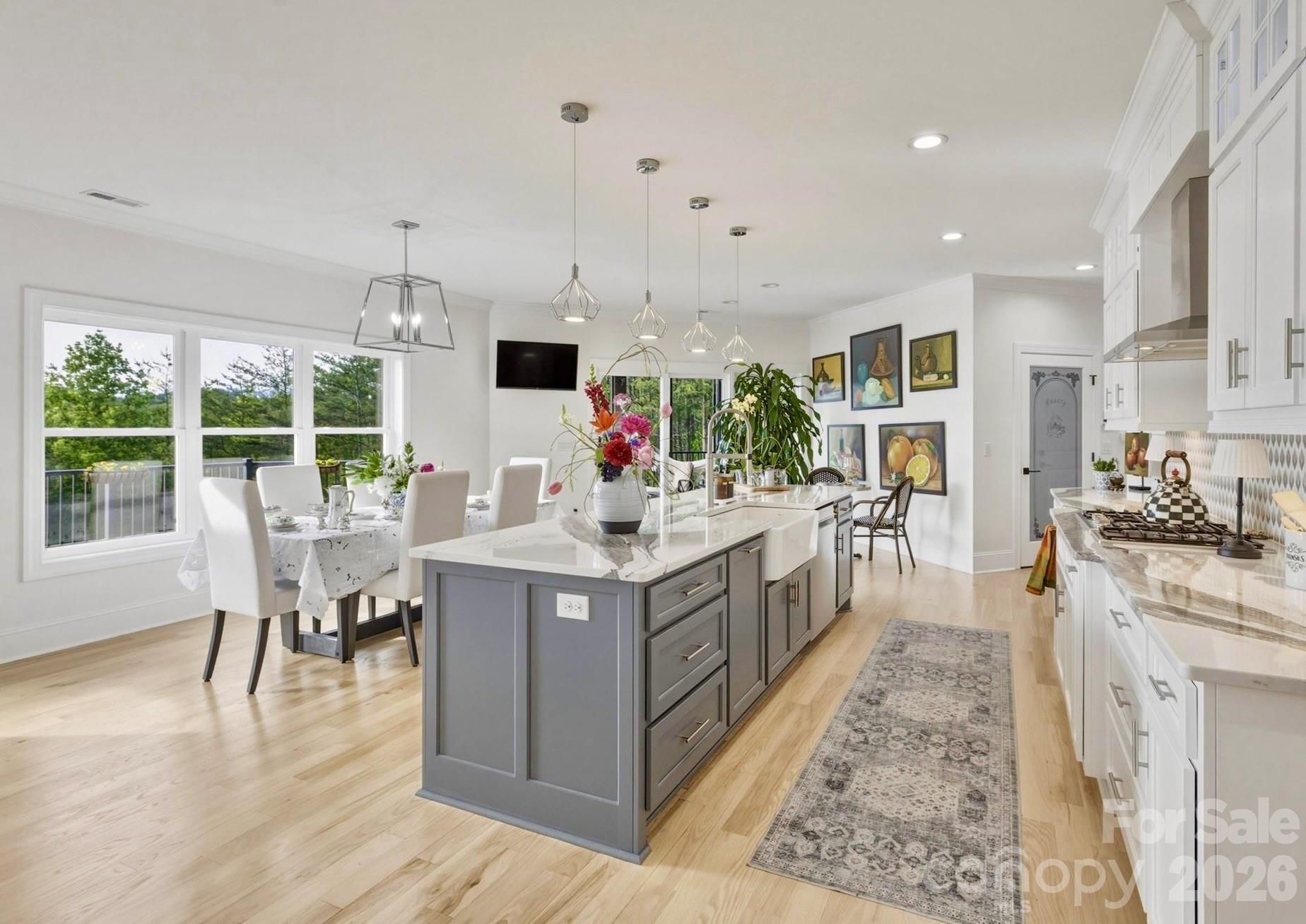 The kitchen is a Foodie's dream space • Luxurious Cambria Quartz countertops throughout the generous work surfaces, dedicated wet bar area, and the island • Under cabinet lighting showcases the unique, eye-catching trompe-l'œil tile backsplash • An elegant Blanco farm sink occupies the +/- 10.5 ft kitchen island with bar seating • Premium Bosch appliances, including wall oven and microwave • Lighted upper transom cabinets with glass doors to showcase decorative items or fine china • A section of floor to ceiling cabinets includes a matching enclosed refrigerator-freezer surround • Behind an etched glass door is a walk-in pantry with upper shelves, lower pull-out shelves, and quartz counter tops • Large kitchen windows create a bright space for the casual dining table, with a backdrop of the majestic Blue Ridge Mountains. - 1506 High Valley Way, Lenoir