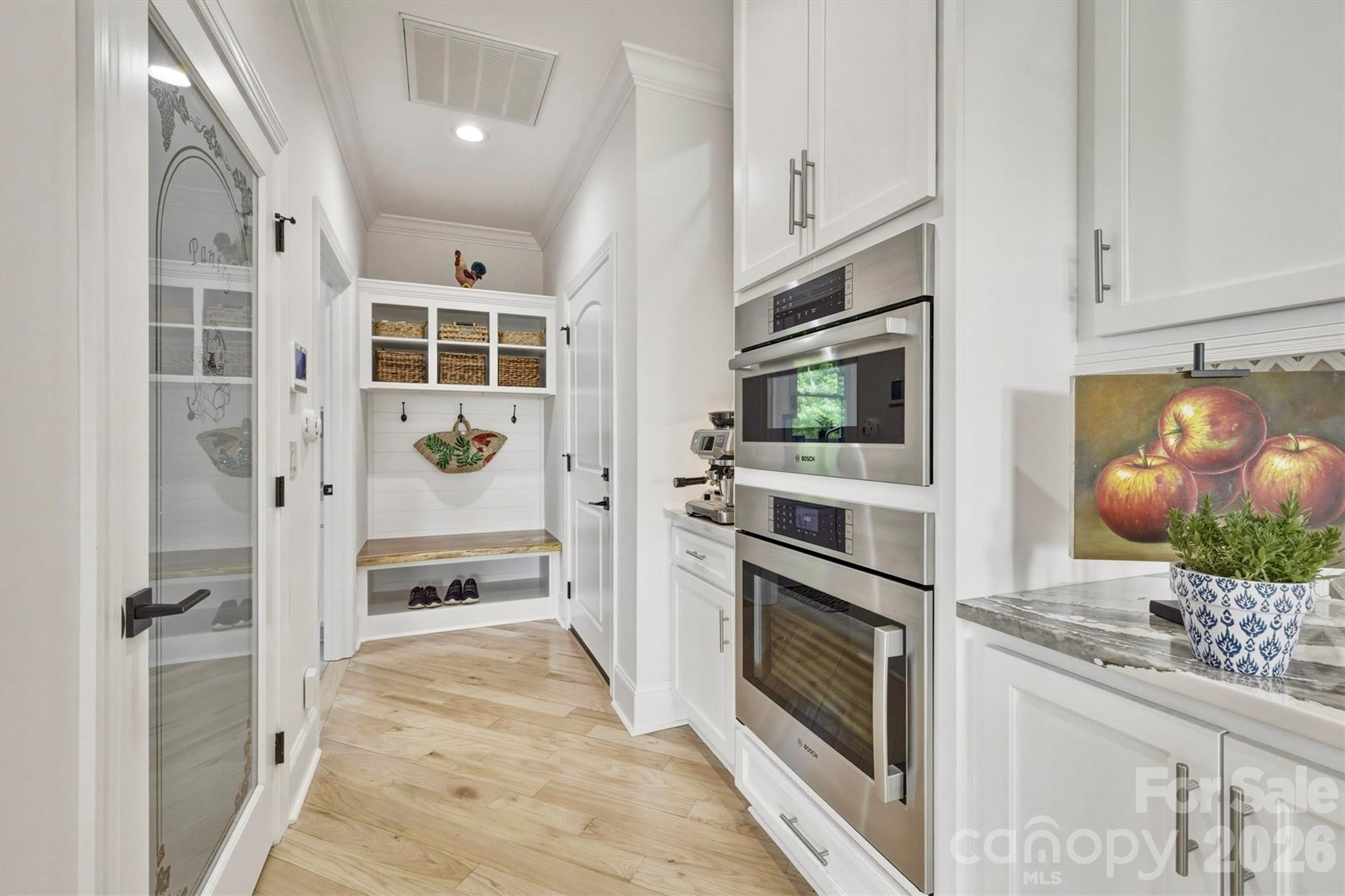 Etched glass door to walk-in pantry on the left. Bosche wall oven and microwave • Beyond the oven is a coffee station, the garage entry, and a built in drop zone with shelf and basket storage, coat hooks, bench and shoe storage. - 1506 High Valley Way, Lenoir