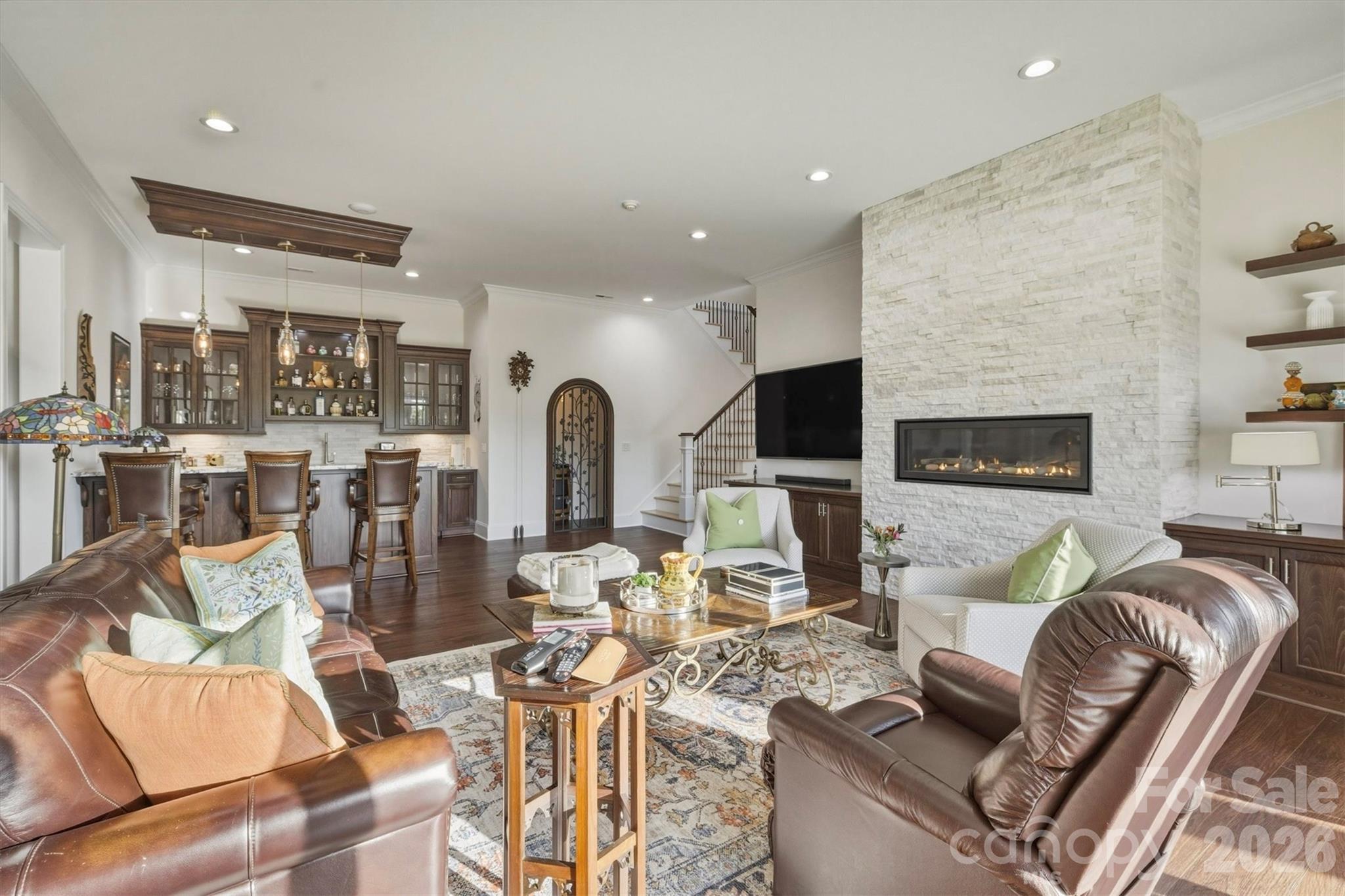 Downstairs, the den has Scandi-style elevated architectural elements and an ambience of refined luxury. 11-foot white walls include a 3-dimensional white stone feature wall with built-in, sleek, linear fireplace. Dark wood alcove cabinets and floating shelves flank the fireplace wall. A bank of four glass doors opens to the porch and mountain view, while sustaining an abundance of natural light. - 1506 High Valley Way, Lenoir