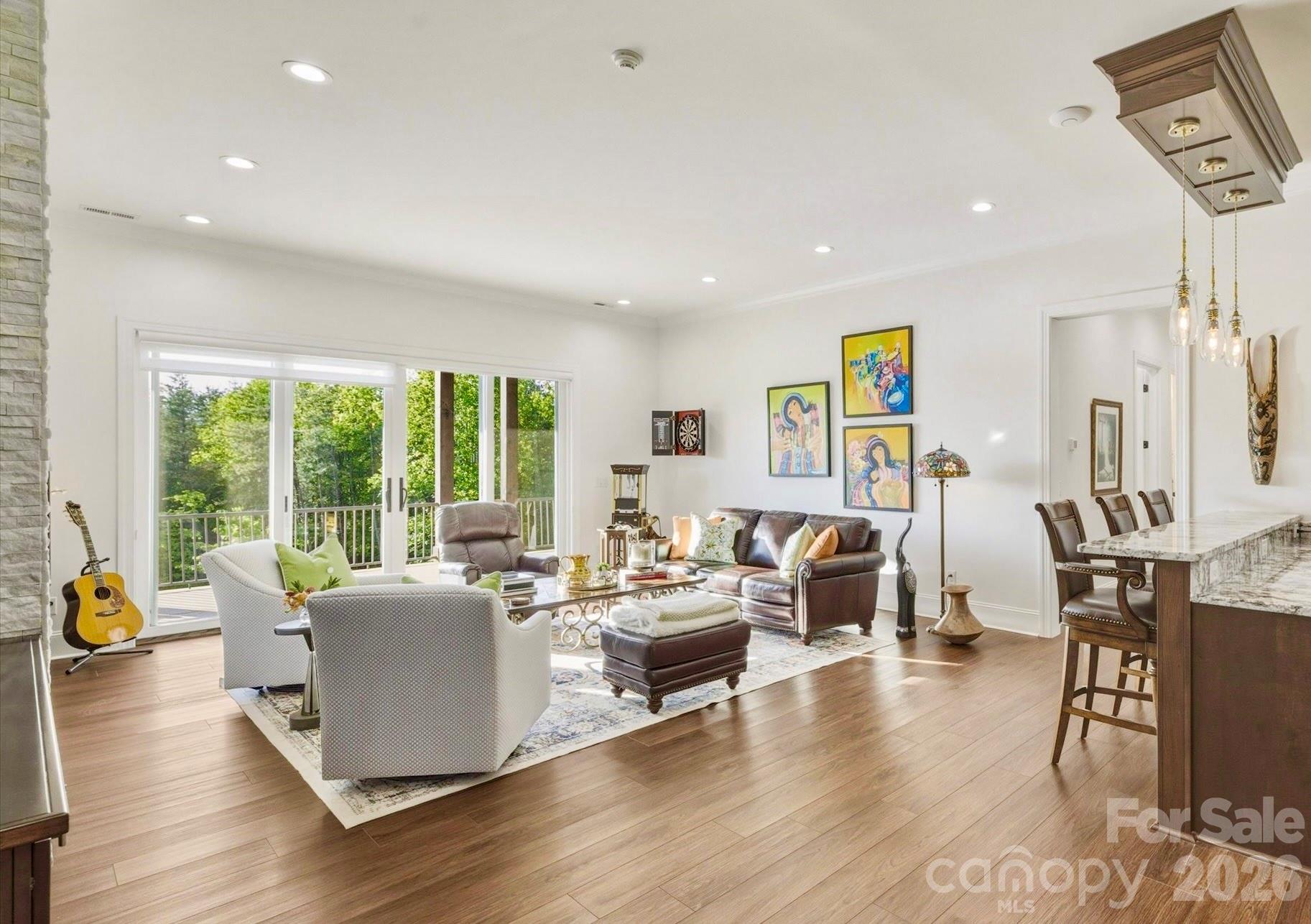 Downstairs, the den has Scandi-style elevated architectural elements and an ambience of refined luxury. 11-foot white walls include a 3-dimensional white stone feature wall with built-in, sleek, linear fireplace. Dark wood alcove cabinets and floating shelves flank the fireplace wall. A bank of four glass doors opens to the porch and mountain view, while sustaining an abundance of natural light. - 1506 High Valley Way, Lenoir