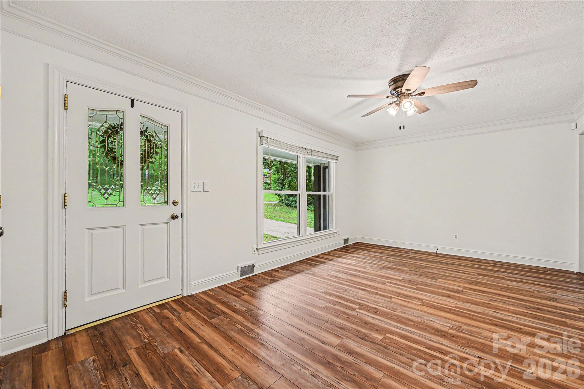 Bright and spacious living room featuring large front windows, crown molding, and durable LVP flooring. - 716 Grandview Drive NE, Concord