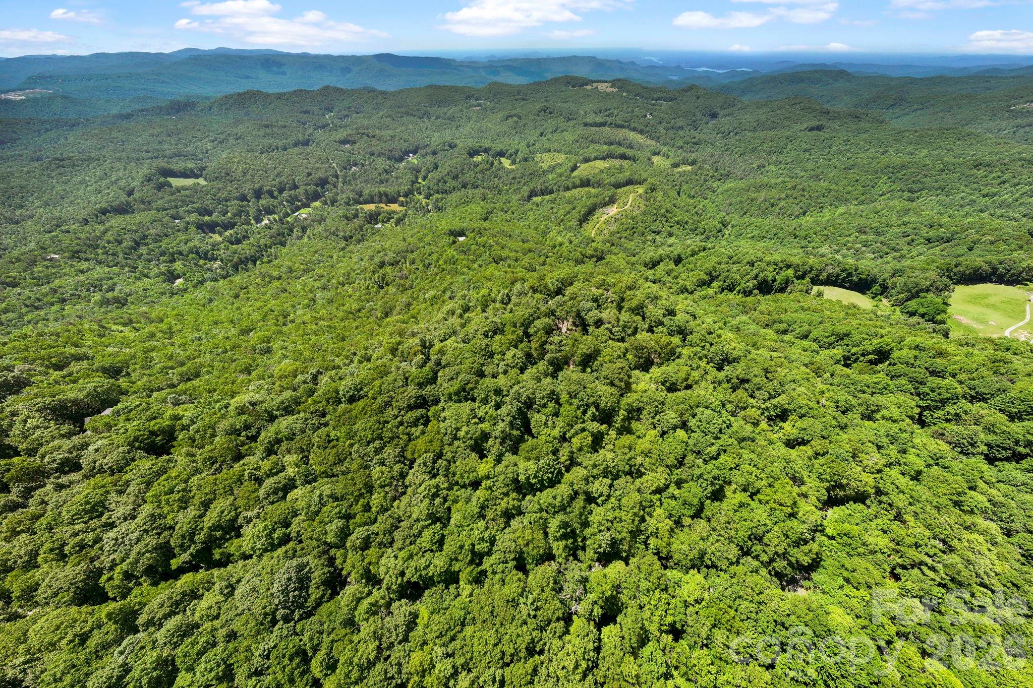 Elevated drone view highlights the property's private mountaintop setting surrounded by expansive forestland and rolling mountain scenery. - 9999 Rocky Mountain Road, Lake Toxaway