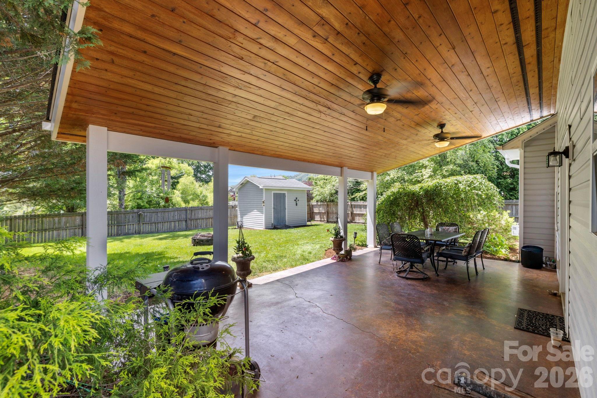 Expansive covered patio with wood-paneled ceiling and ceiling fans, creating an ideal outdoor living and entertaining space. - 266 Wildbriar Road, Fletcher