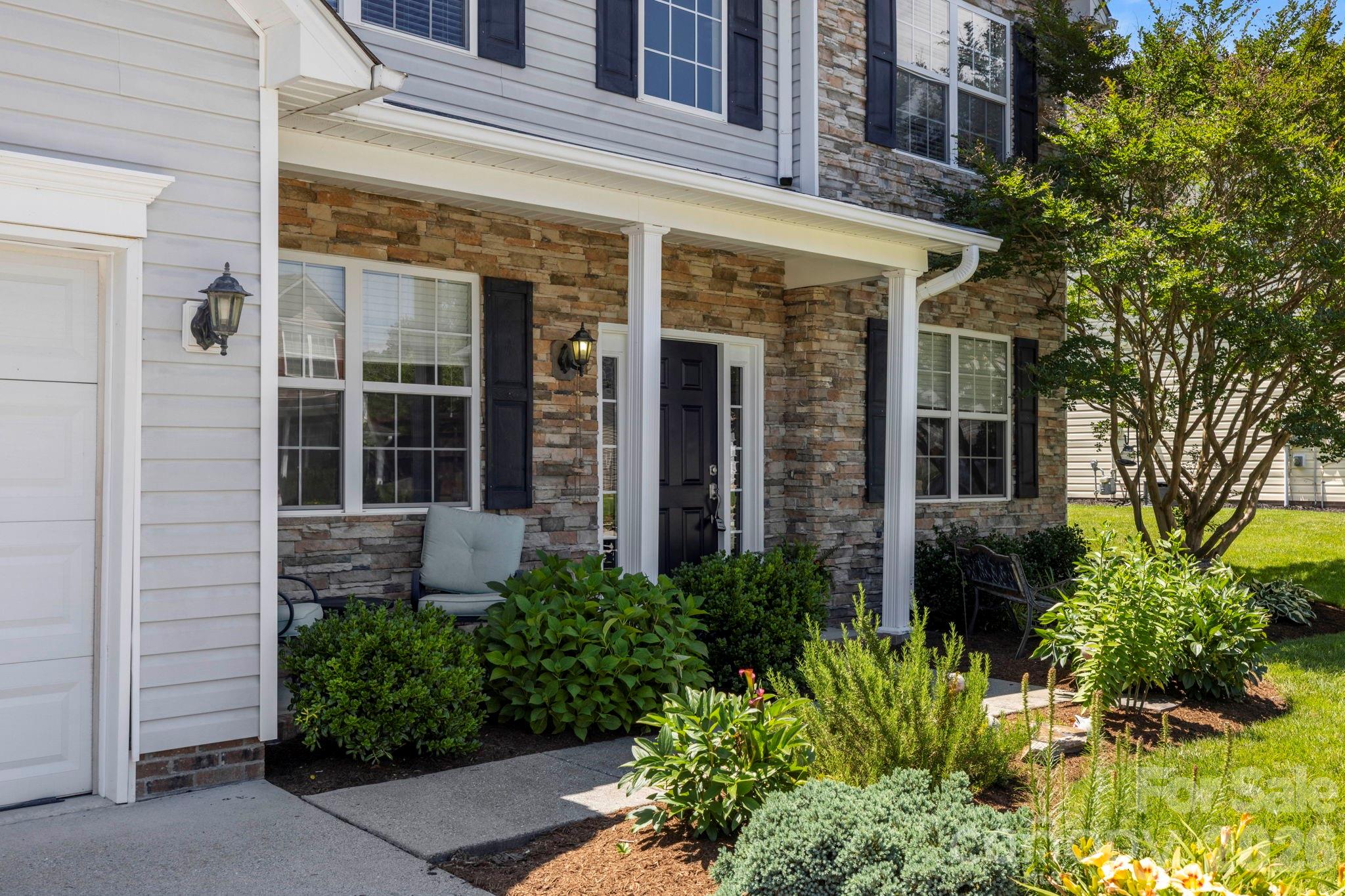 Welcoming covered front porch surrounded by established landscaping, offering a comfortable place to relax and greet guests. - 266 Wildbriar Road, Fletcher
