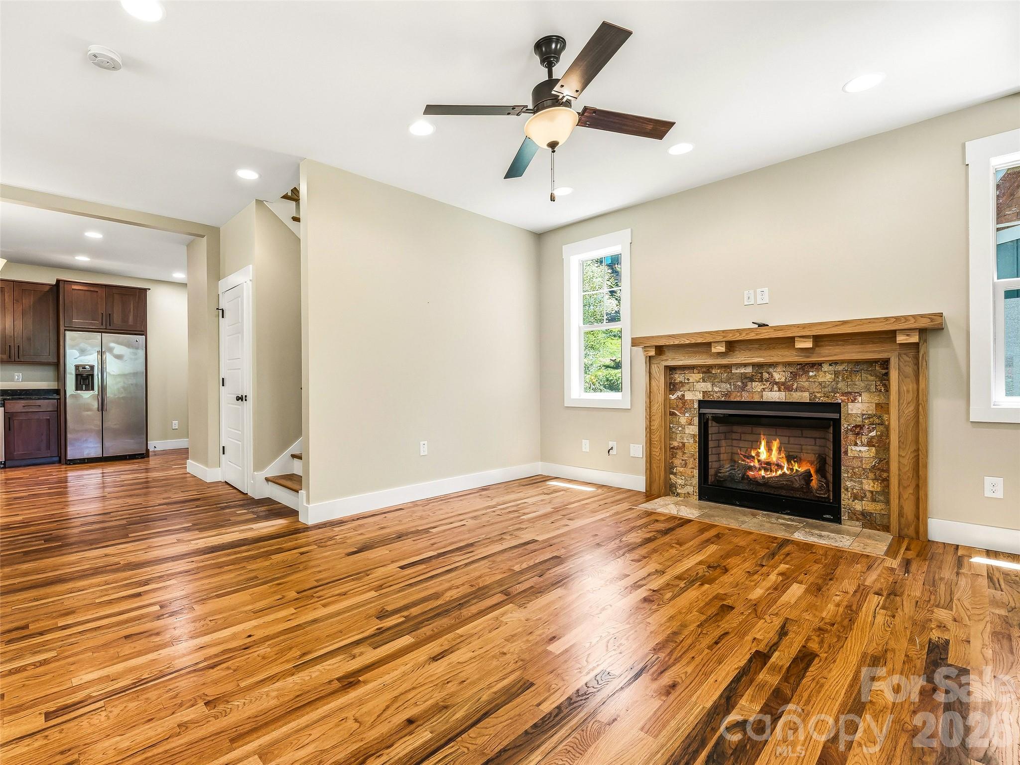 Bright, open-concept living area showcasing gorgeous wood flooring and a cozy gas-log fireplace. - 25 Shady Park Lane, Asheville