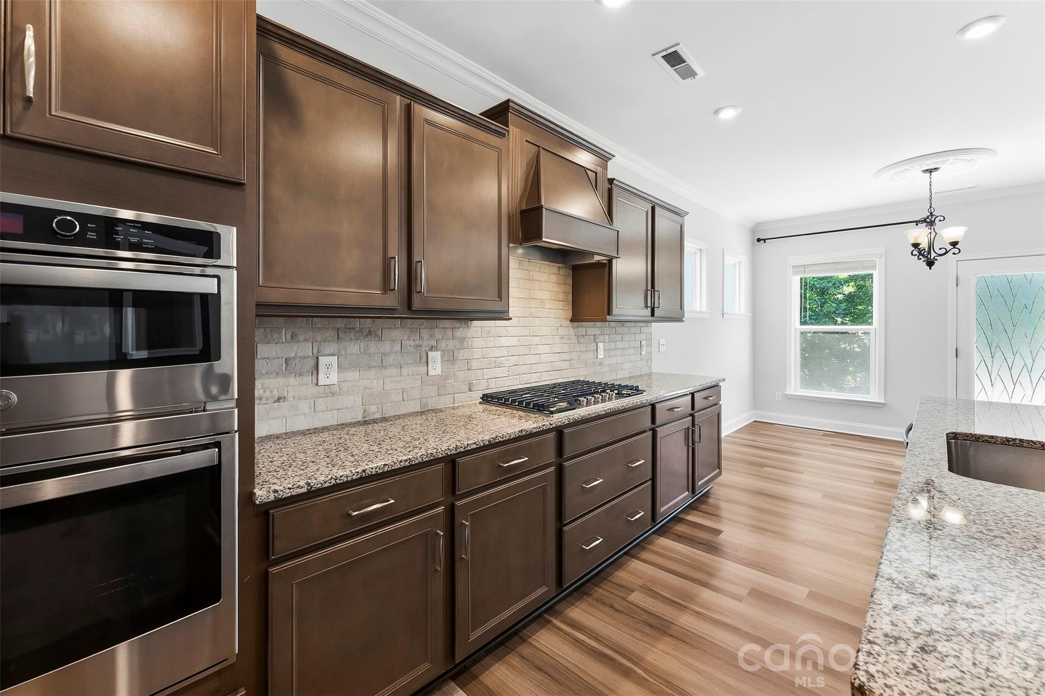 Sleek and stylish cabinetry with designer vent hood, upgraded cabinetry, granite, tile backsplash and. built in appliances featuring microwave/oven combo and gas range. - 1318 Poppy Way, Matthews