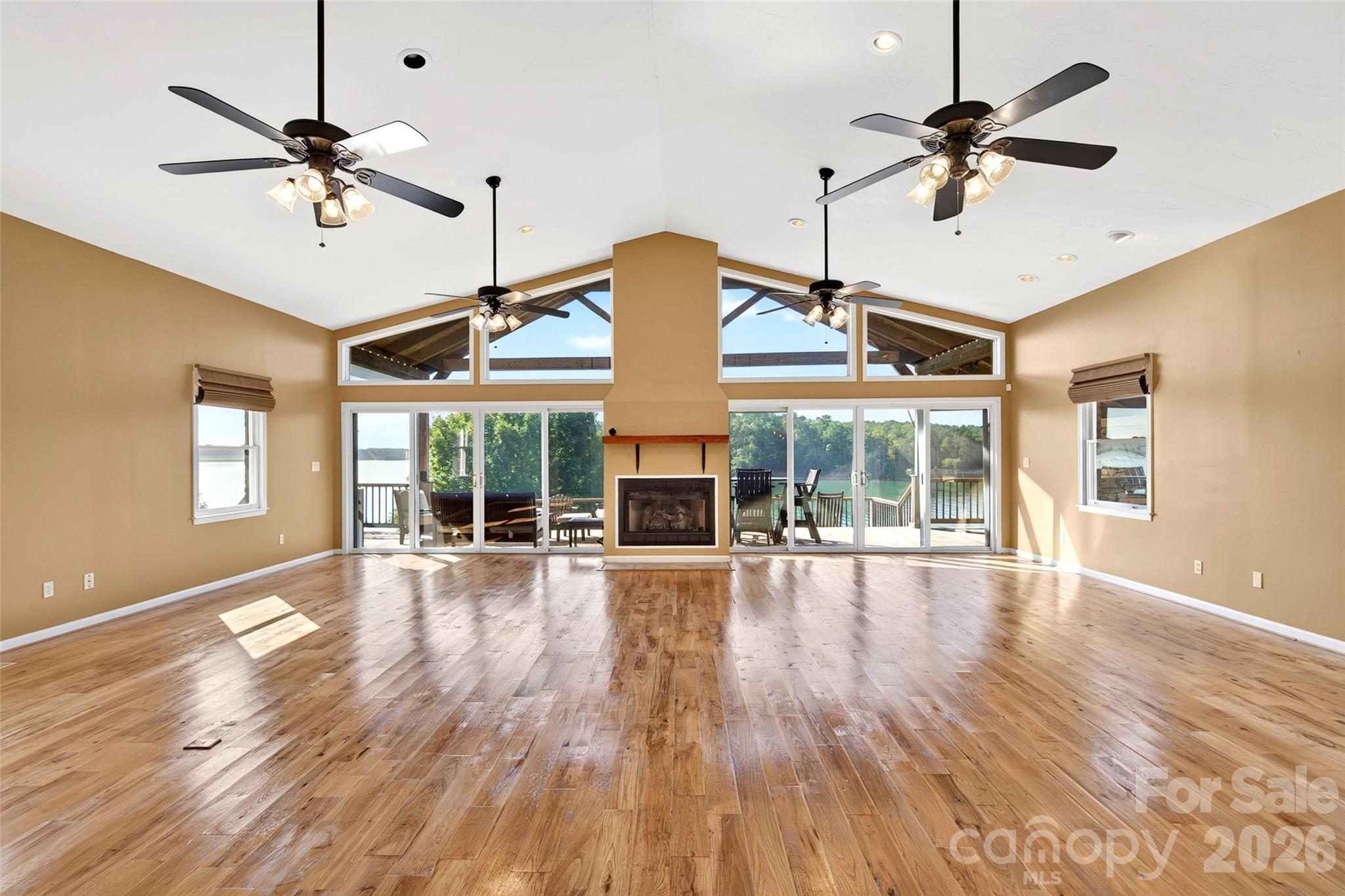Main-level living room with vaulted ceiling, hickory hardwood floors, gas-log fireplace, and lake-side glass. - 831 Lake Club Drive, Nebo