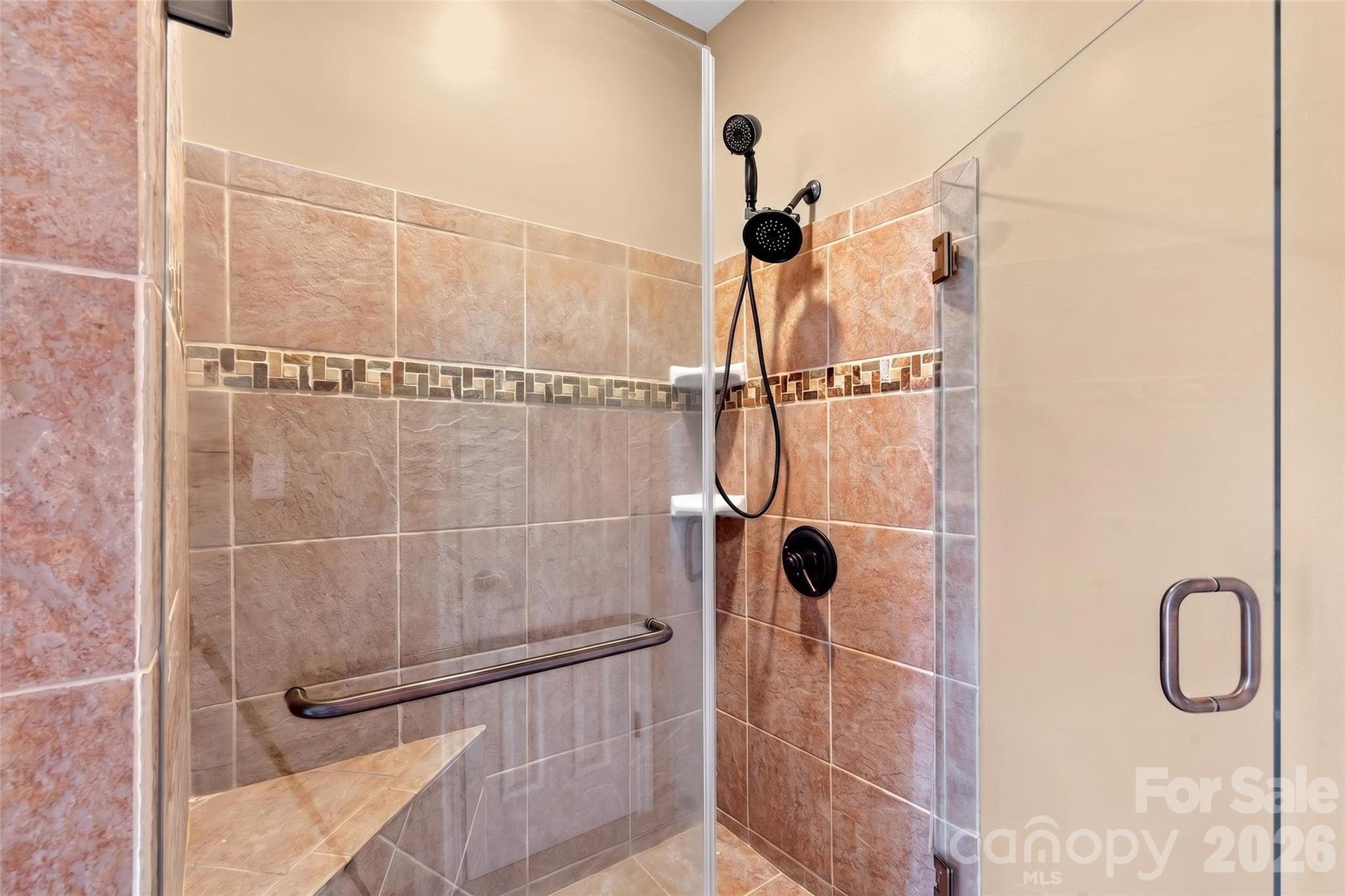 Tiled walk-in shower with bench seating and grab bars in the lower-level bath. - 831 Lake Club Drive, Nebo