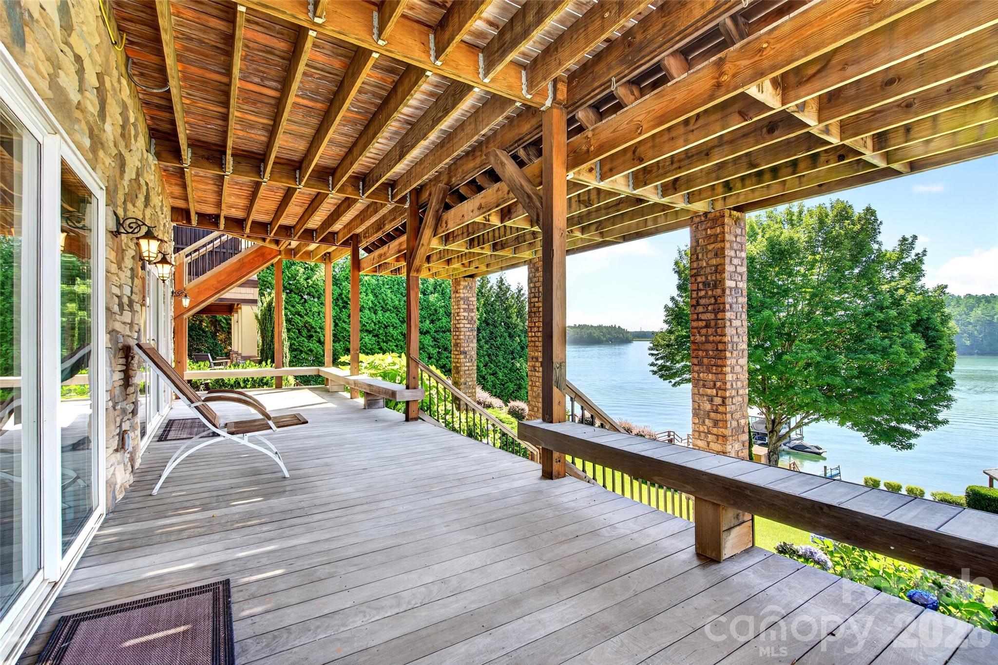 Covered lower patio with stone columns opening to the lawn and Lake James shoreline. - 831 Lake Club Drive, Nebo