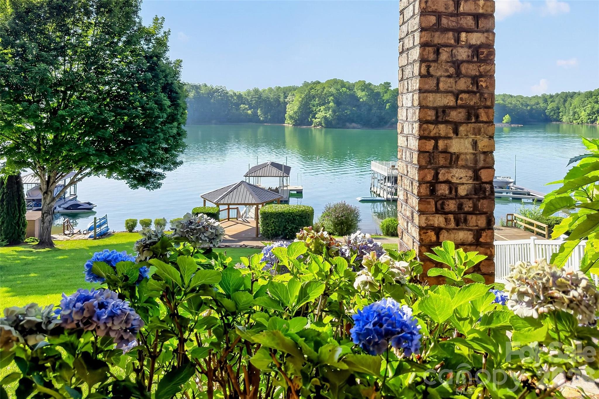 Landscaped lawn with hydrangeas and stone chimney framing the view down to the private dock. - 831 Lake Club Drive, Nebo