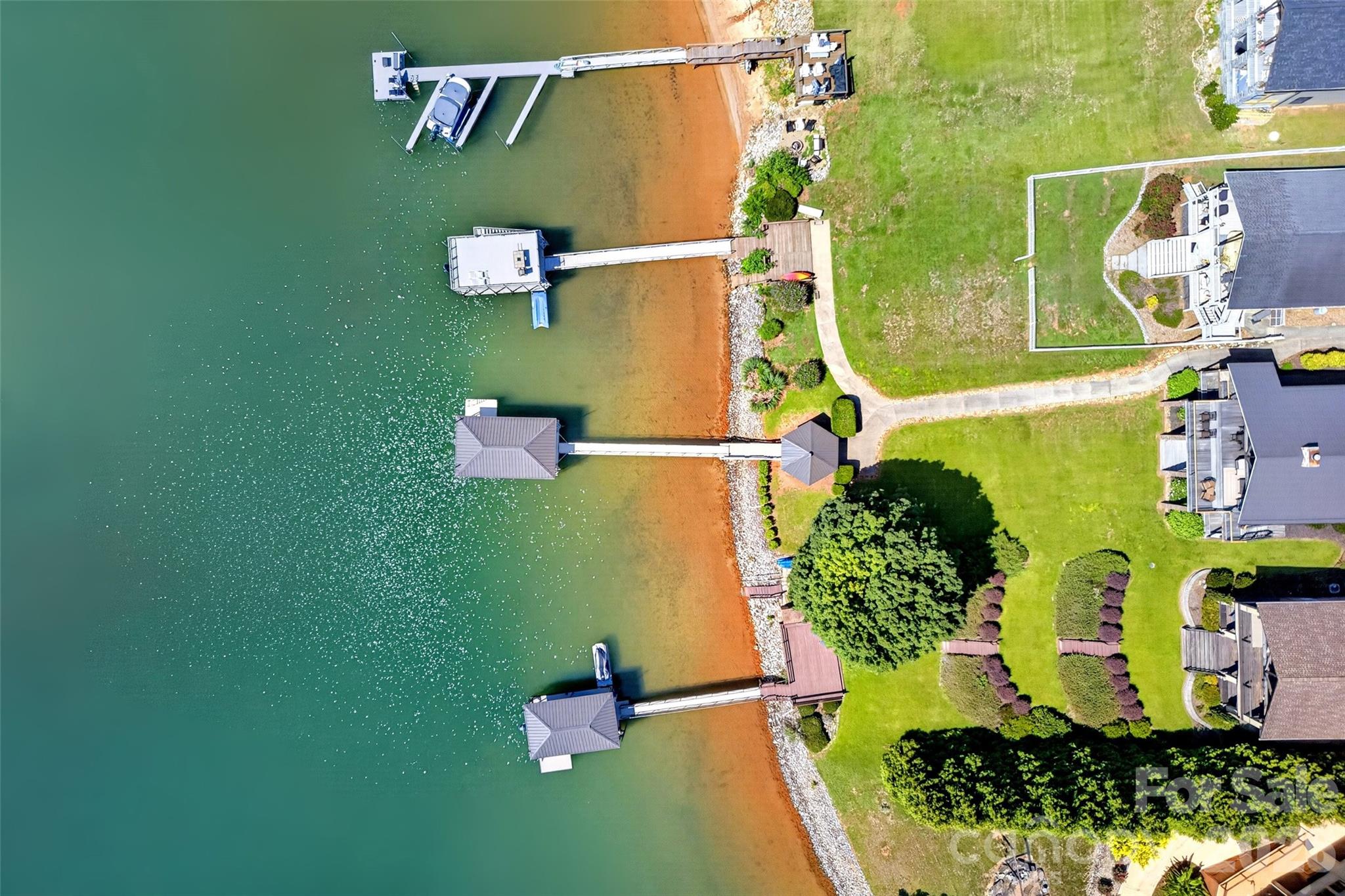 View from the water of the private dock with boat lift, sun deck, and level shoreline lawn. - 831 Lake Club Drive, Nebo