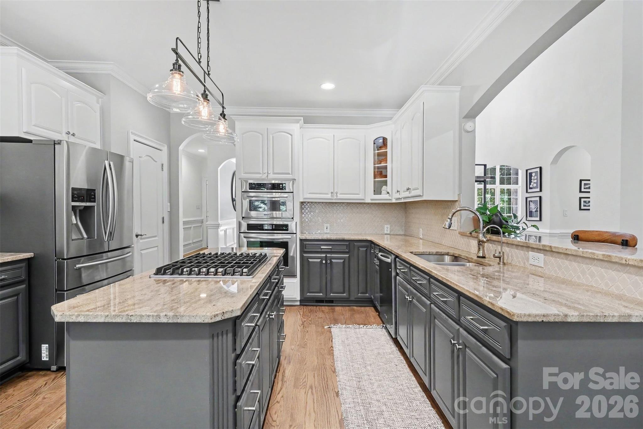 Refreshed designer kitchen featuring two-tone cabinetry, granite countertops, tile backsplash, center island with gas cook top, wall ovens, pantry, and under-sink water filtration. - 109 Whiterock Drive, Mount Holly