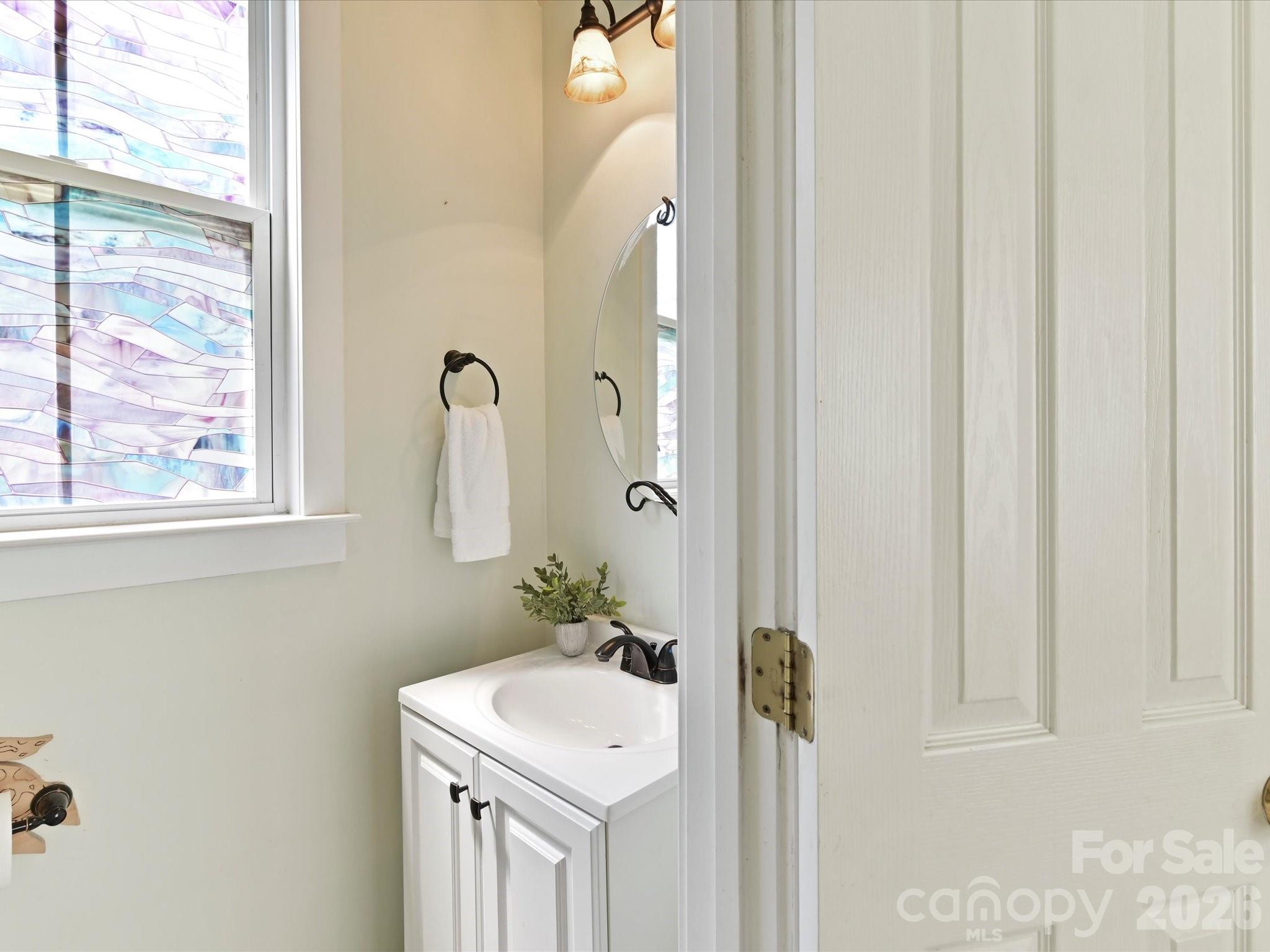 The convenient main-level powder room features a vanity with storage and a window that brings in natural light, providing added comfort for guests and everyday living. - 13106 Kennerly Drive, Huntersville