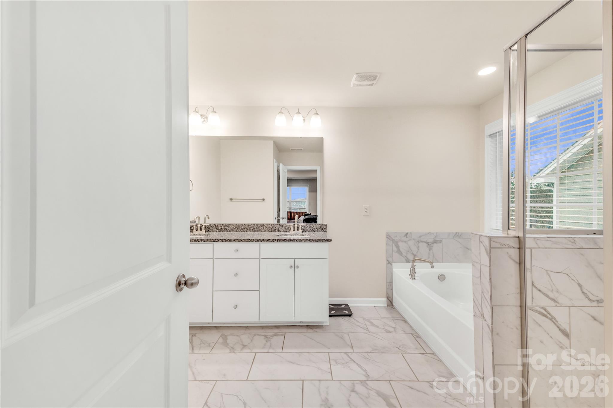 This stunning primary en-suite showcases a dual vanity with granite counters, beautiful marble-look time flooring and matching tile surrounds. - 4849 Tacoma Drive, Fort Mill