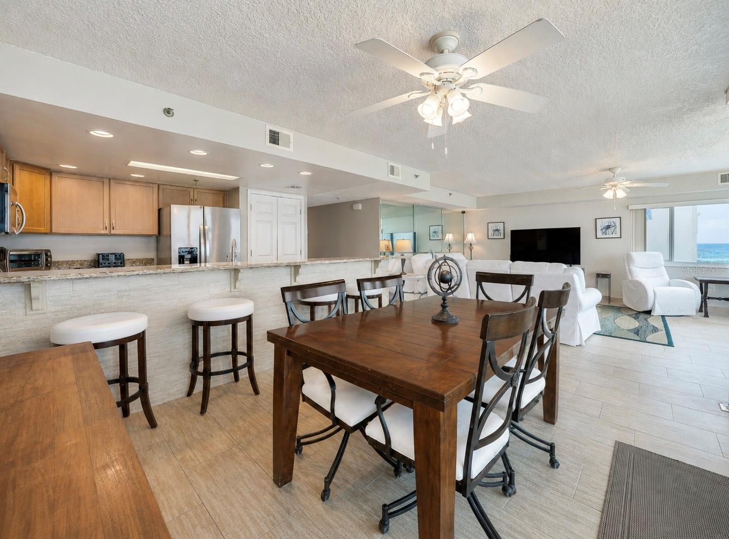 A central dining area connects to the kitchen and living space, all under ceiling fans and surrounded by windows—ideal for casual meals and gatherings. - 6727 TURTLEMOUND RD #315, NEW SMYRNA BEACH