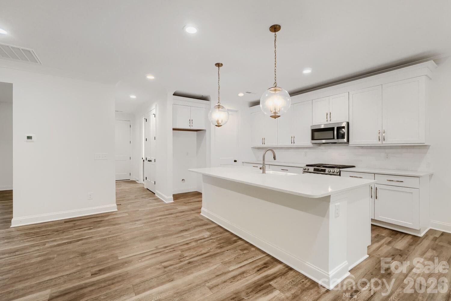 The heart of the home shines with white shaker cabinets, gold hardware, and stainless appliances. A large island with pendant lighting opens seamlessly to the main living area. - 2358 Fay Jones Road, Denver