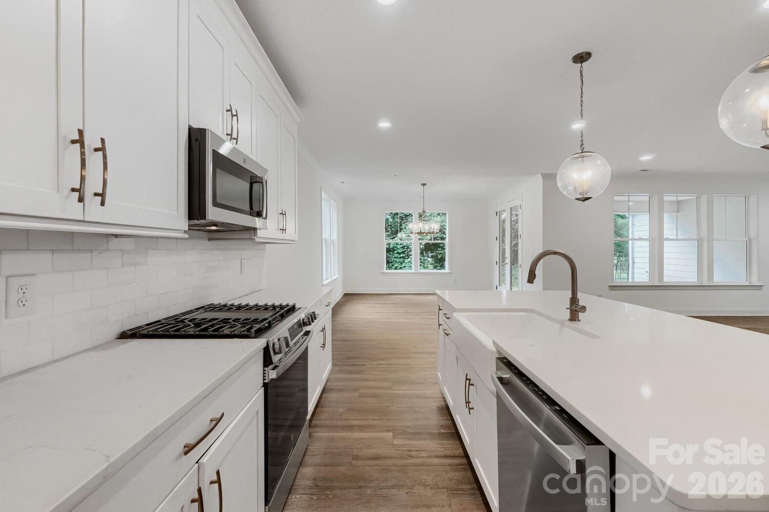 A stunning kitchen with a center island, globe pendant lights, and gold-accented hardware. It opens to a sunlit dining nook with a classic chandelier. - 2358 Fay Jones Road, Denver