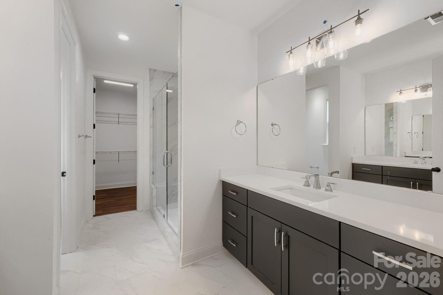 The primary bath offers a dual-vanity setup with contemporary gray cabinetry and a glass-enclosed marble shower. A walk-in closet just off the vanity adds everyday convenience. - 2358 Fay Jones Road, Denver