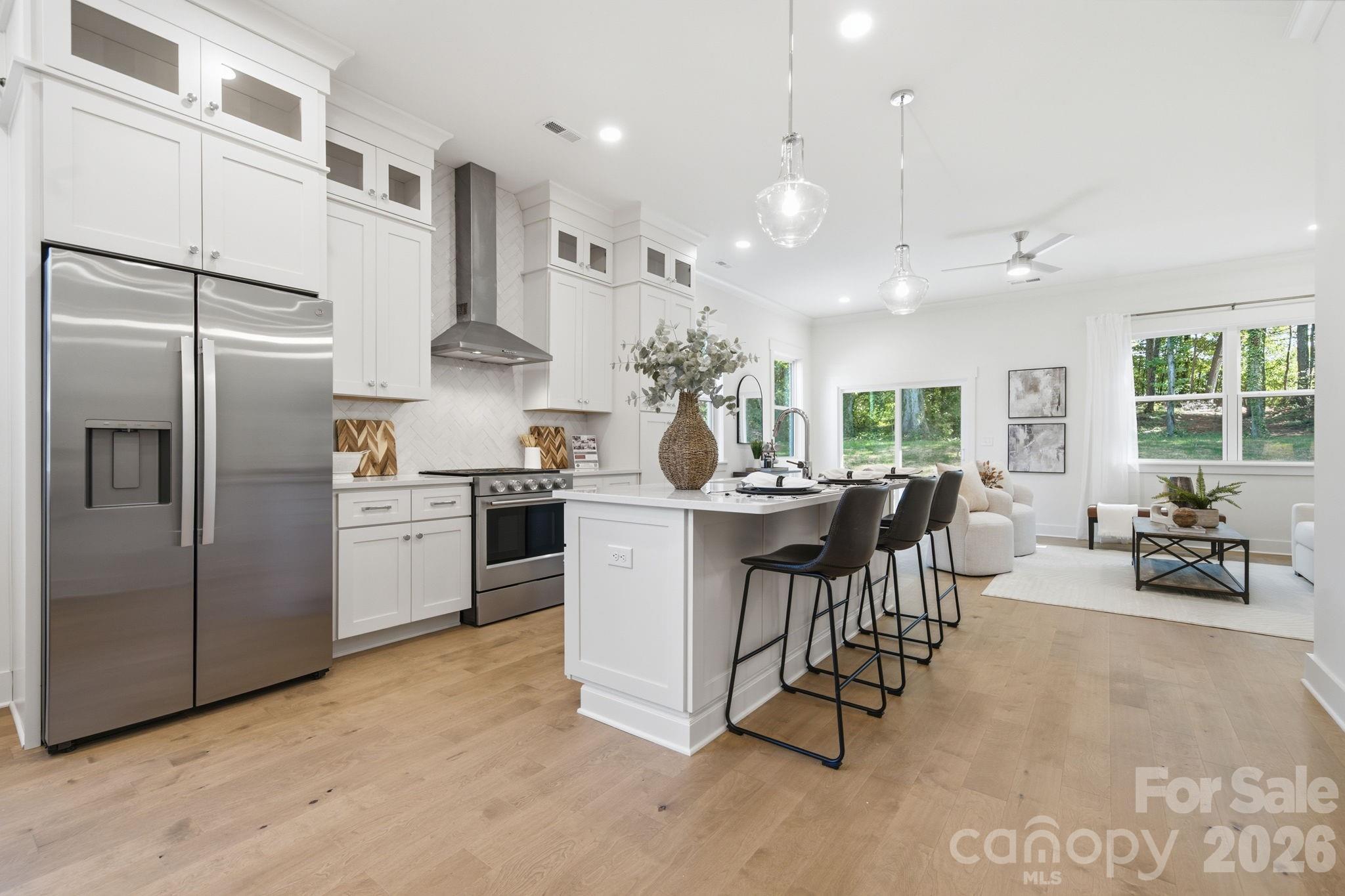 The bright, open kitchen features quartz countertops, beautiful flat iron bianco herringbone backsplash, ceiling-height stacked cabinets, a large island, gas range, walk-in pantry, & upgraded KitchenAid appliances - 612 Camelot Drive, Salisbury
