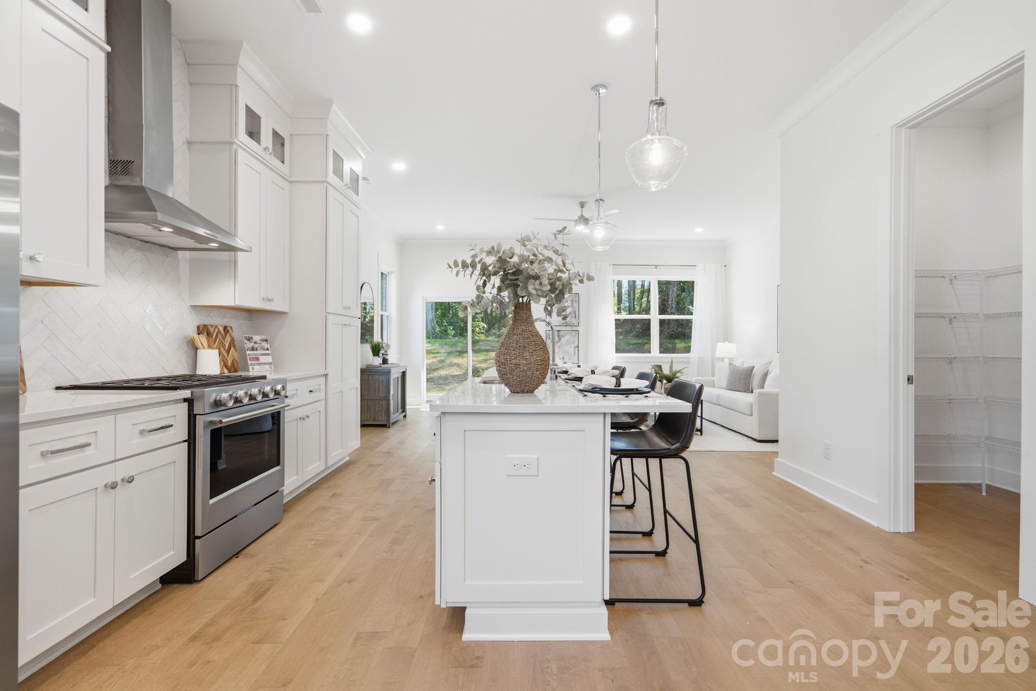 The bright, open kitchen features quartz countertops, beautiful flat iron bianco herringbone backsplash, ceiling-height stacked cabinets, a large island, gas range, walk-in pantry, & upgraded KitchenAid appliances - 612 Camelot Drive, Salisbury