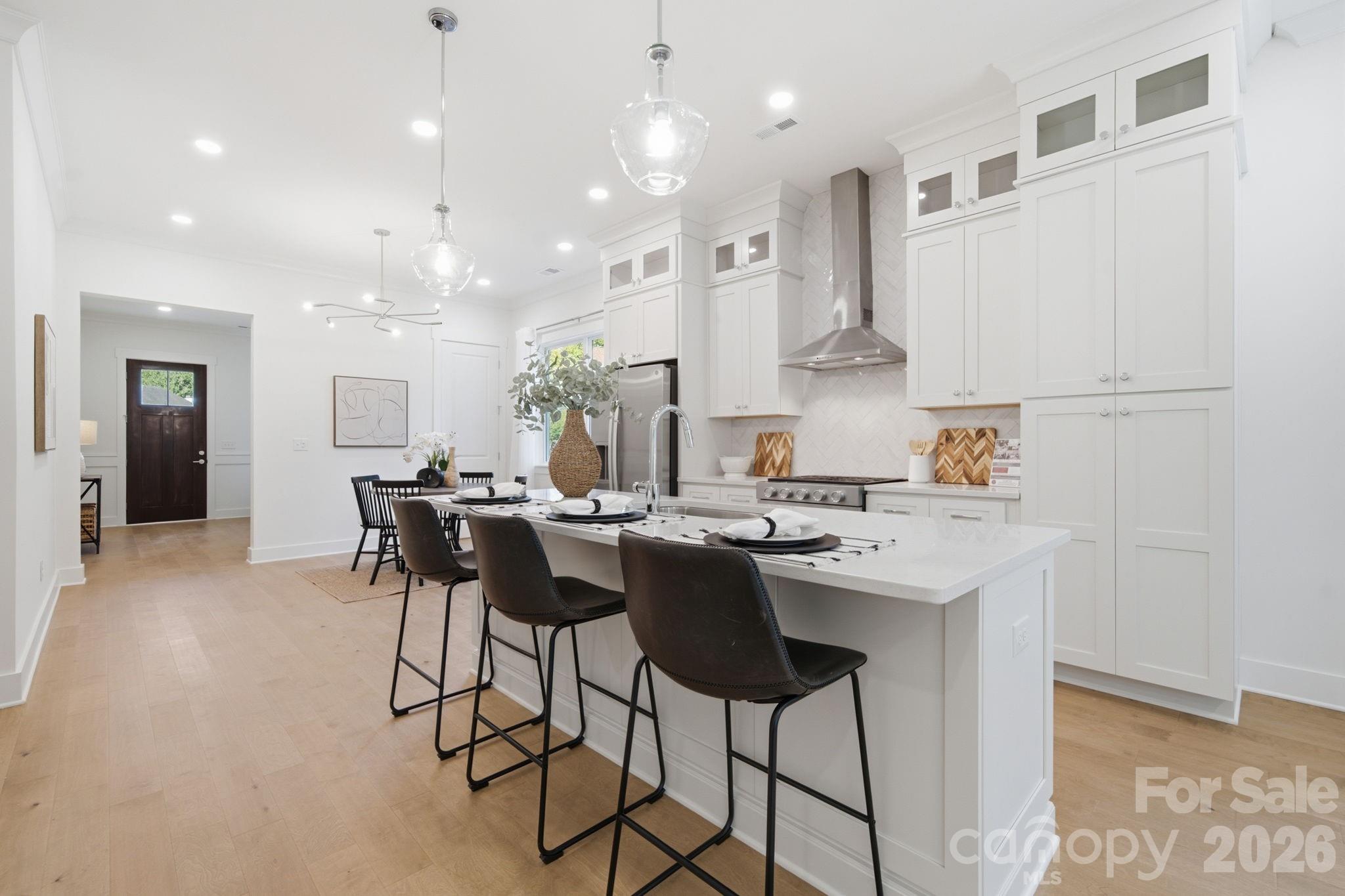 The bright, open kitchen features quartz countertops, beautiful flat iron bianco herringbone backsplash, ceiling-height stacked cabinets, a large island, gas range, walk-in pantry, & upgraded KitchenAid appliances - 612 Camelot Drive, Salisbury