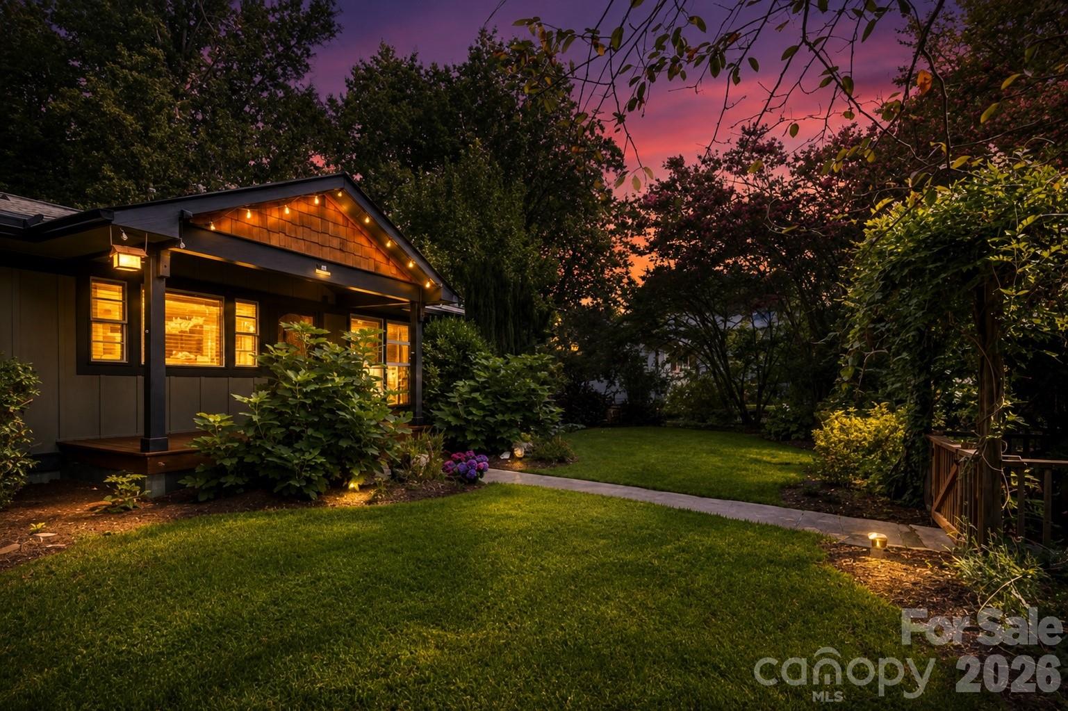 Twilight view highlighting the home’s warm window glow, charming eave lighting and lush, private setting. Virtually twilight edited. - 10 Davenport Place, Asheville