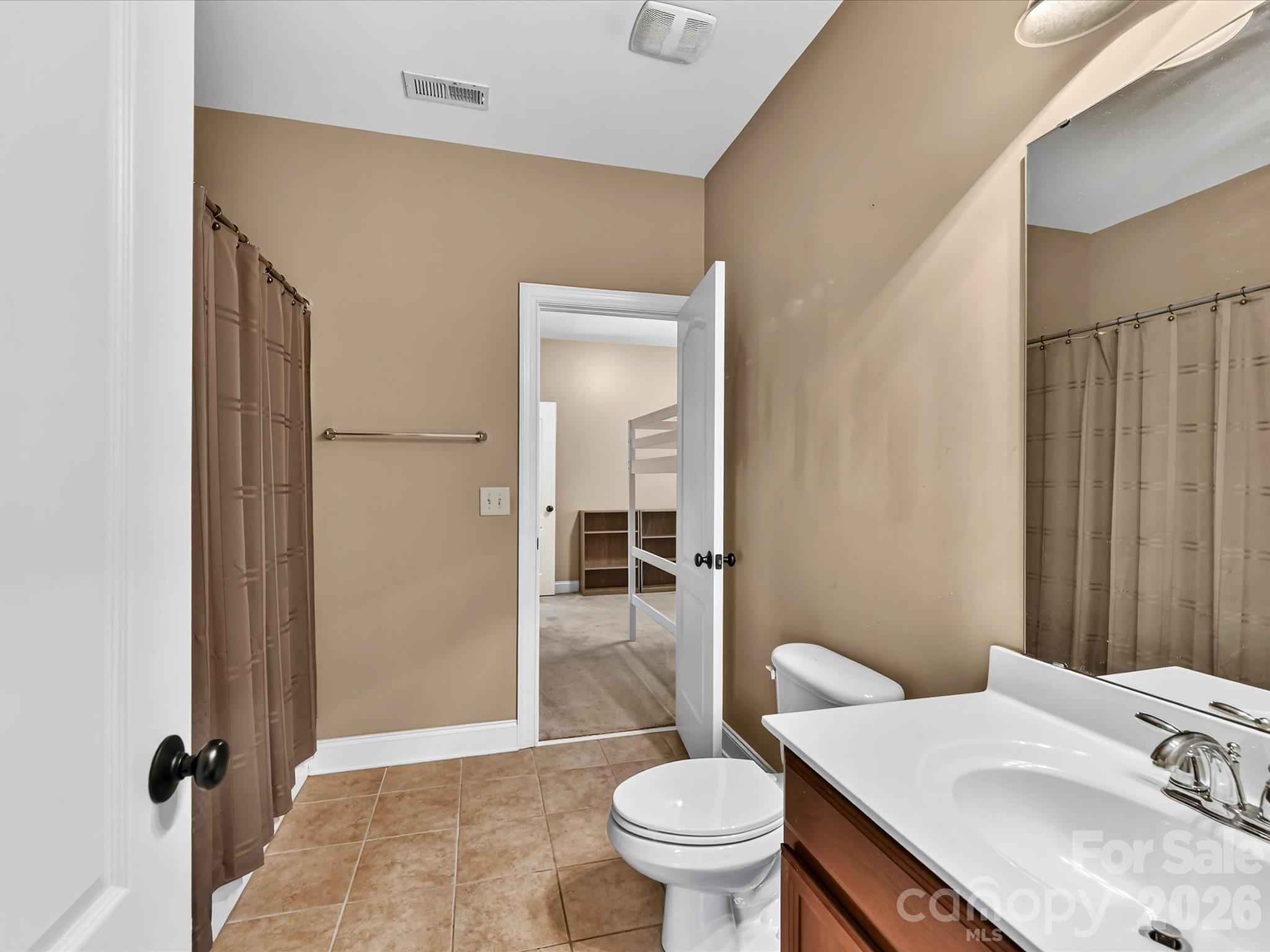 Bright secondary bathroom featuring a spacious vanity, tiled flooring, and a tub/shower combination with convenient access to the adjoining bedroom. - 11203 Warfield Avenue, Huntersville