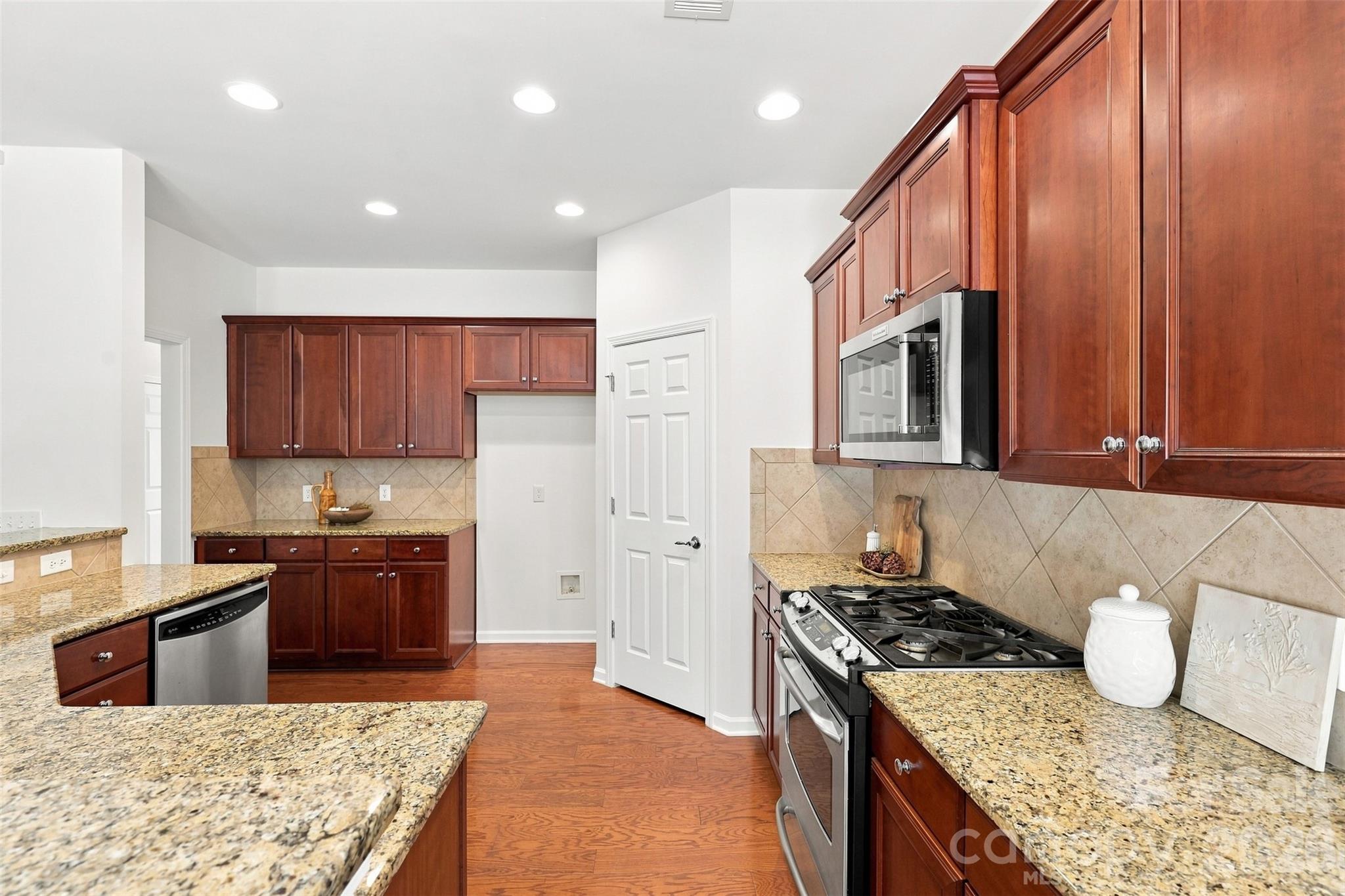 Well-appointed kitchen features rich wood cabinetry, granite countertops, a tiled backsplash, stainless steel appliances and recessed lighting - 10345 Scotland Avenue, Indian Land