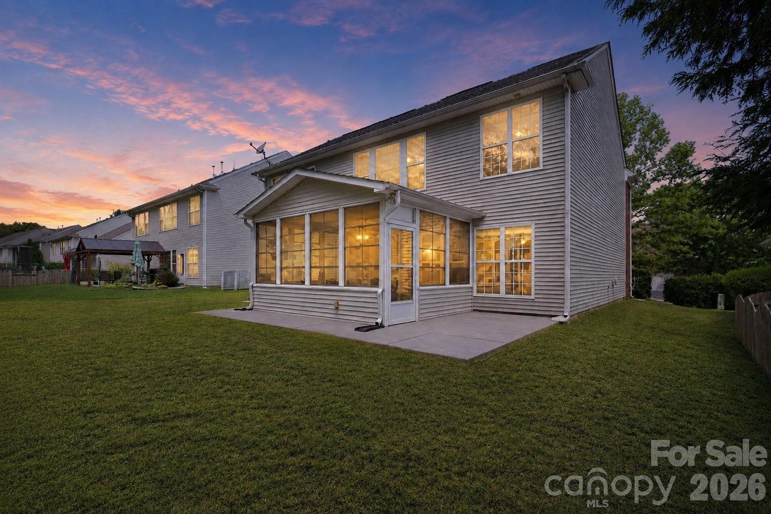Beautiful twilight view showcases the warmly illuminated rear exterior and four-seasons room beneath a colorful evening sky - 10345 Scotland Avenue, Indian Land