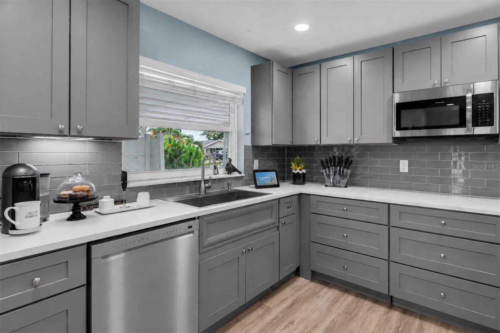 Updated kitchen features gray custom cabinetry with soft-close drawers, quartz countertops and sleek gray tile backsplash. - 7891 4TH AVE S, ST PETERSBURG
