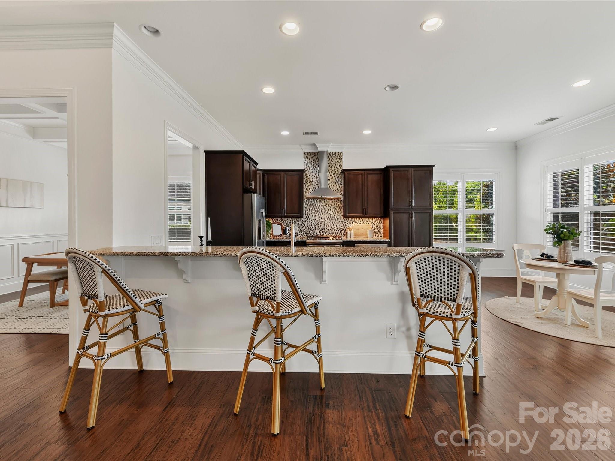Spacious kitchen features granite countertops, abundant cabinetry, stainless steel appliances, a gas range with vent hood, decorative tile backsplash, and an expansive breakfast bar with seating. - 13003 Riley Grace Lane, Cornelius