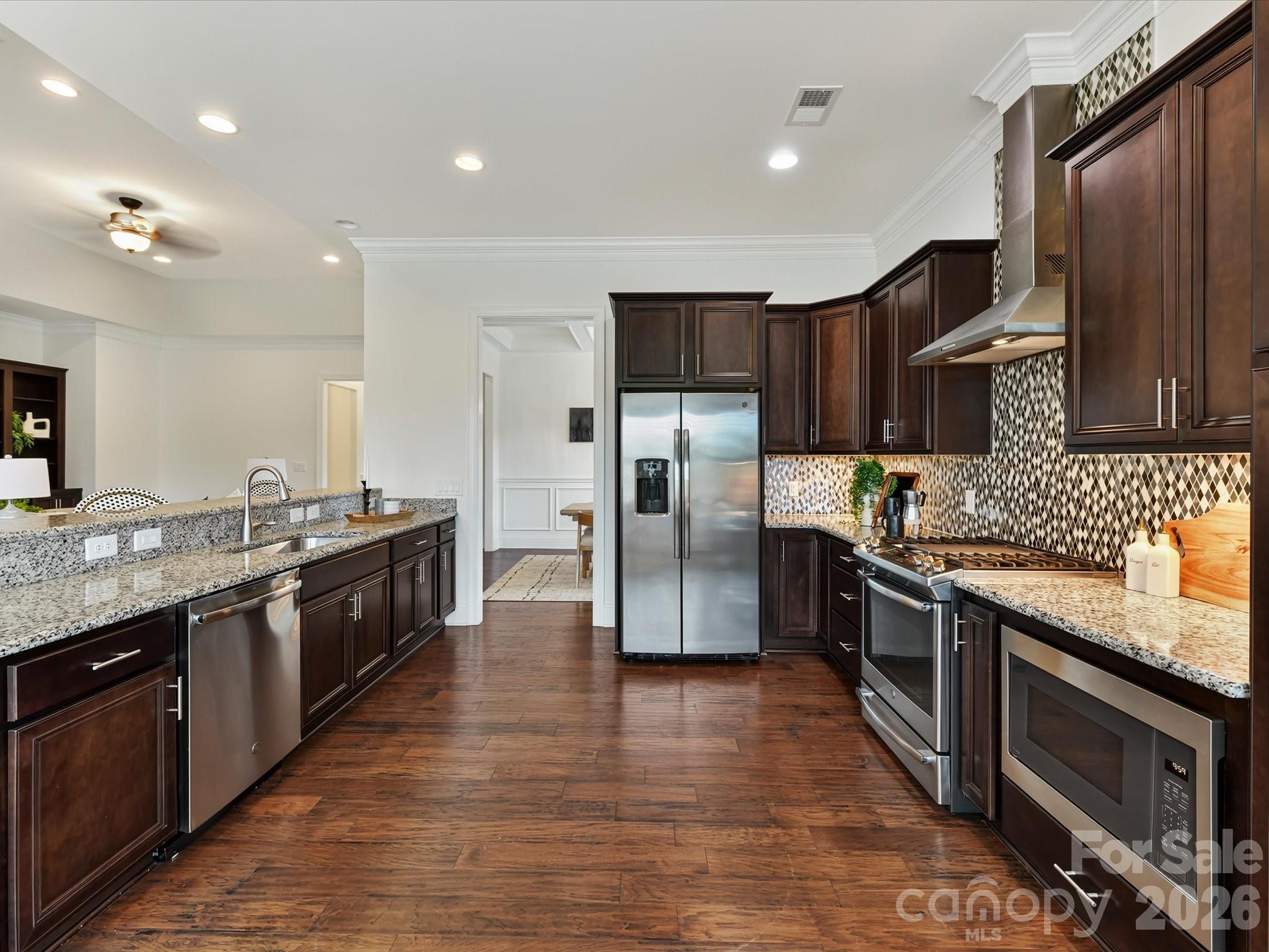 Spacious kitchen features granite countertops, abundant cabinetry, stainless steel appliances, a gas range with vent hood, decorative tile backsplash, and an expansive breakfast bar with seating. - 13003 Riley Grace Lane, Cornelius